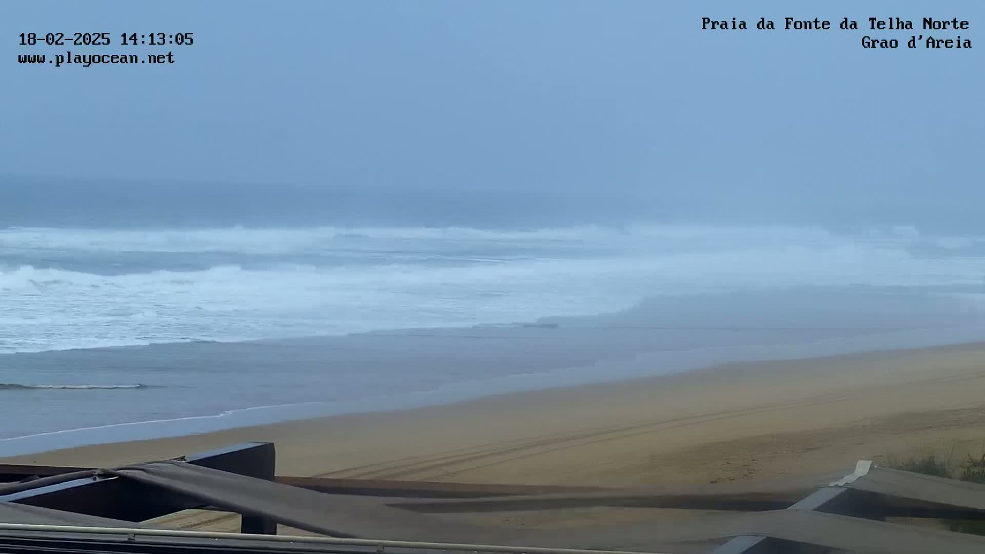 A hazy, overcast day reveals a sandy beach and moderately sized waves rolling into the shore.