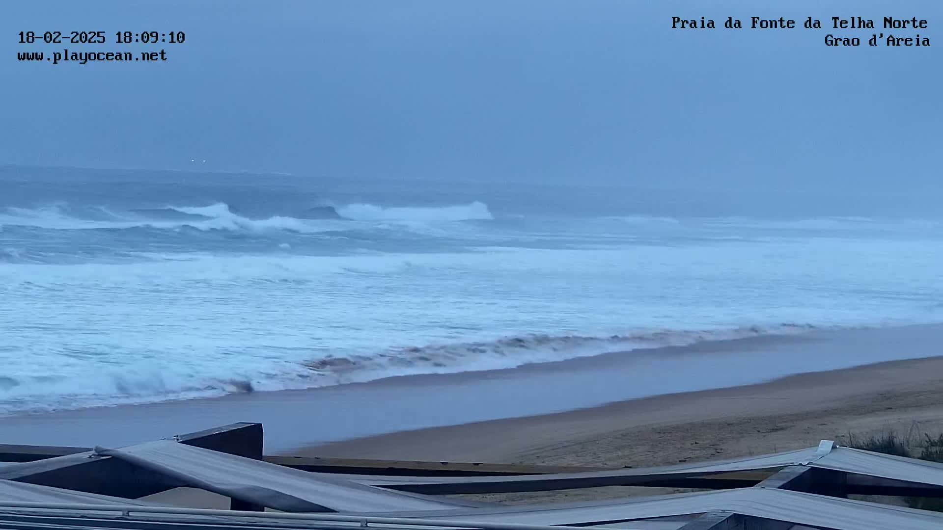 A sandy beach with moderate waves rolling onto the shore under an overcast sky.