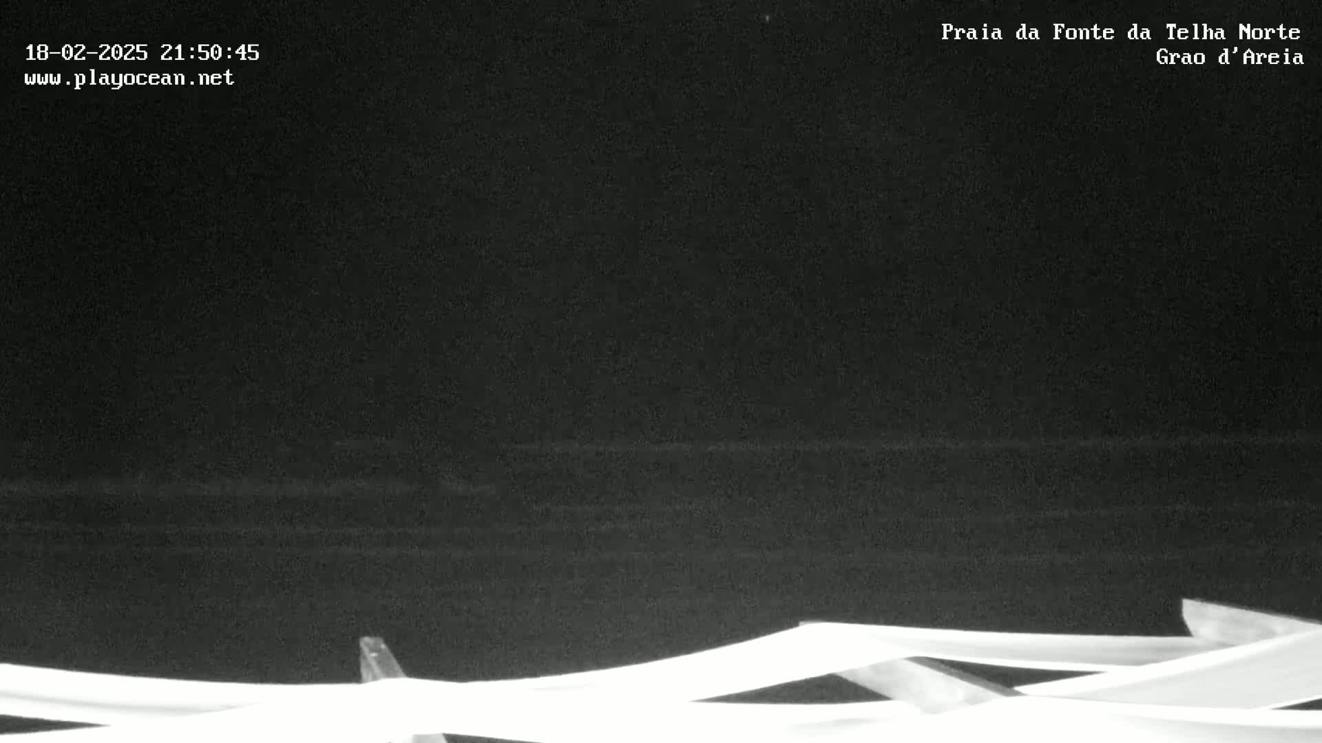 A nighttime, low-light view of a dark ocean with a structure of white bars in the foreground.