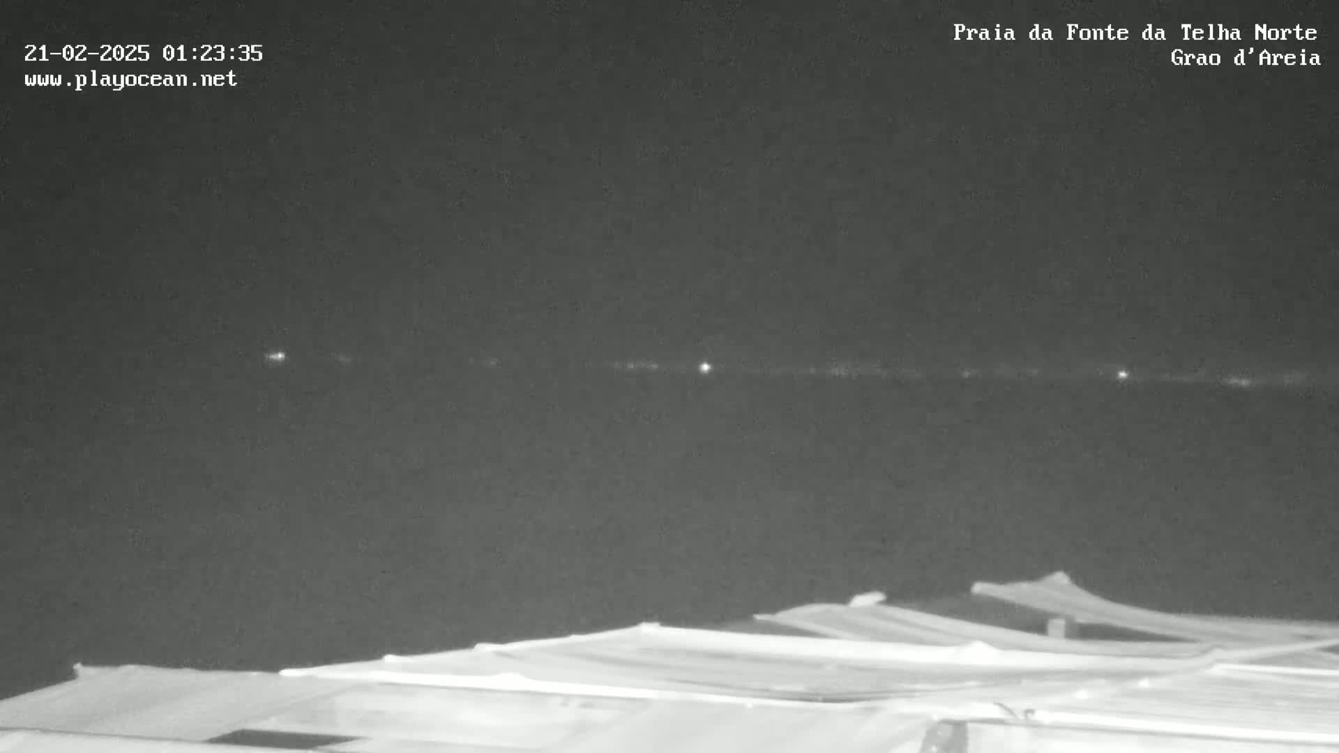 A nighttime view shows a dark body of water with faint lights on the horizon, above a row of low structures.