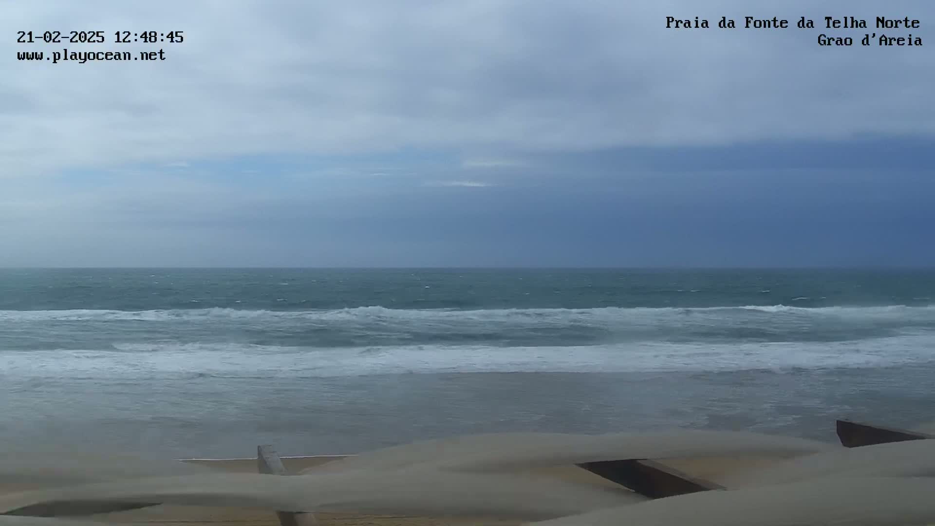 A view of a beach with moderately rough ocean waves under an overcast sky.