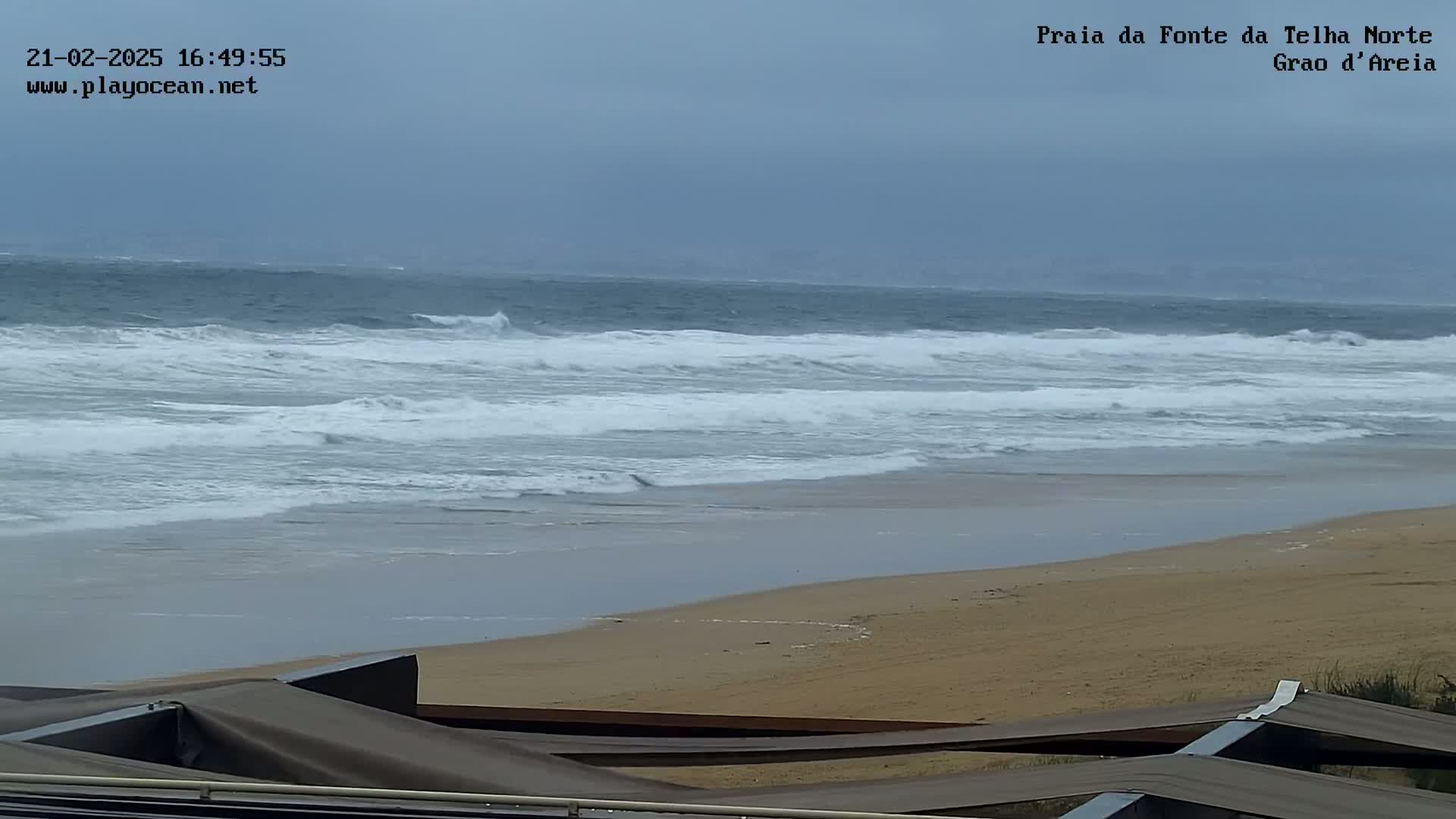 A sandy beach with moderately sized waves rolling in under an overcast sky.