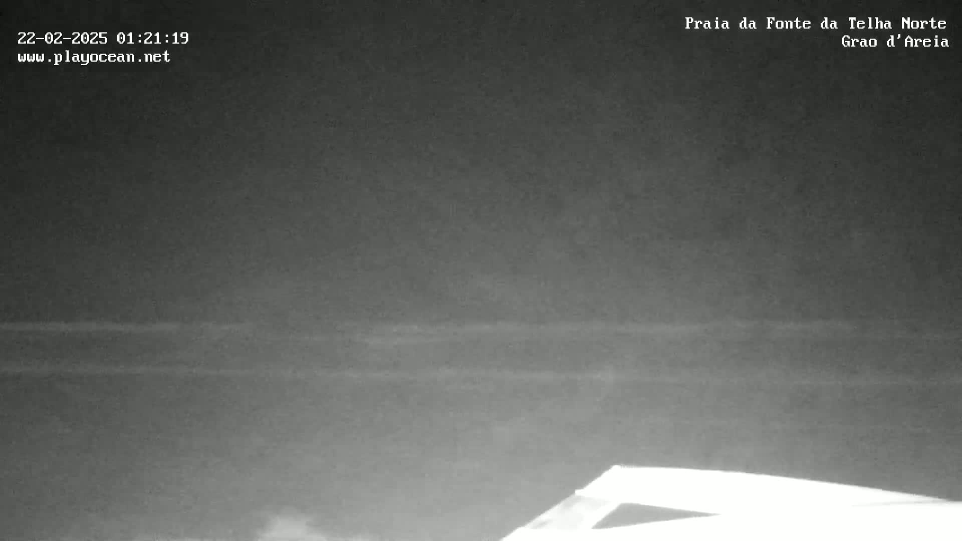 A low-light, nighttime image shows a dark beach or body of water with faint, horizontal lines possibly indicating waves or ripples.