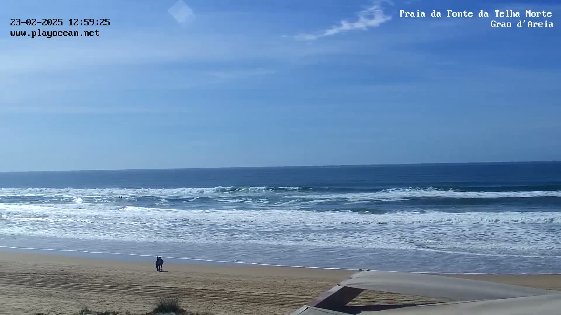 A sandy beach with gentle waves under a mostly clear blue sky.