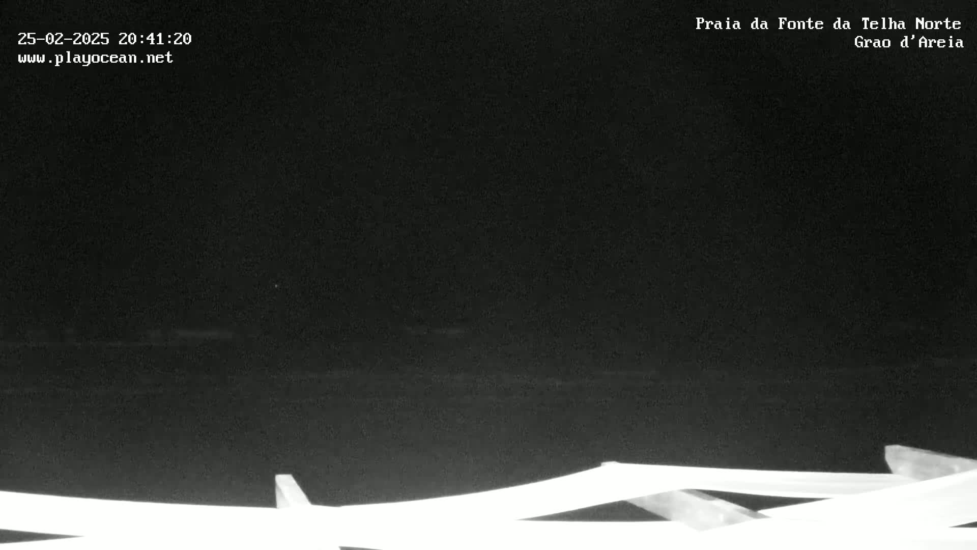 A nighttime, low-light image shows a dark body of water and a portion of a white railing in the lower foreground.