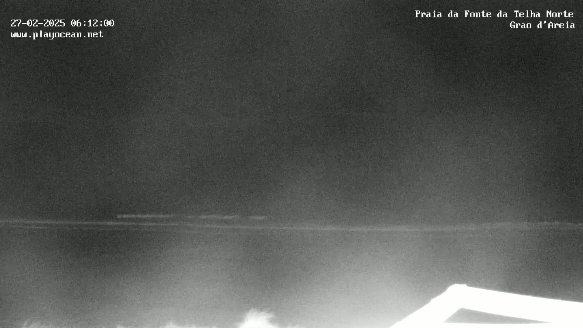 A dark, nighttime beach scene shows a faint, barely visible horizon line with a slightly lighter area suggesting the ocean.