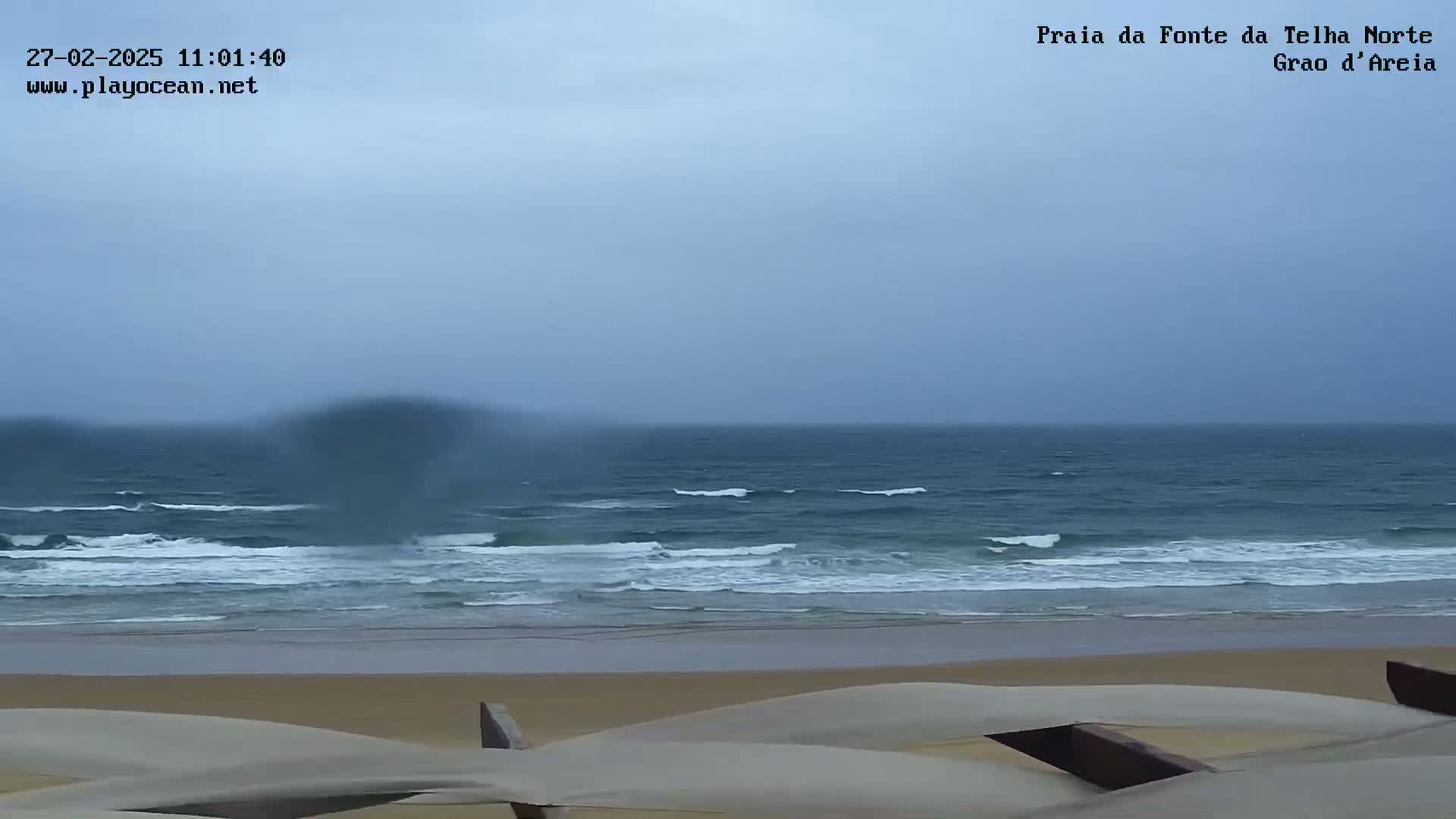 A sandy beach with moderate waves under an overcast sky.