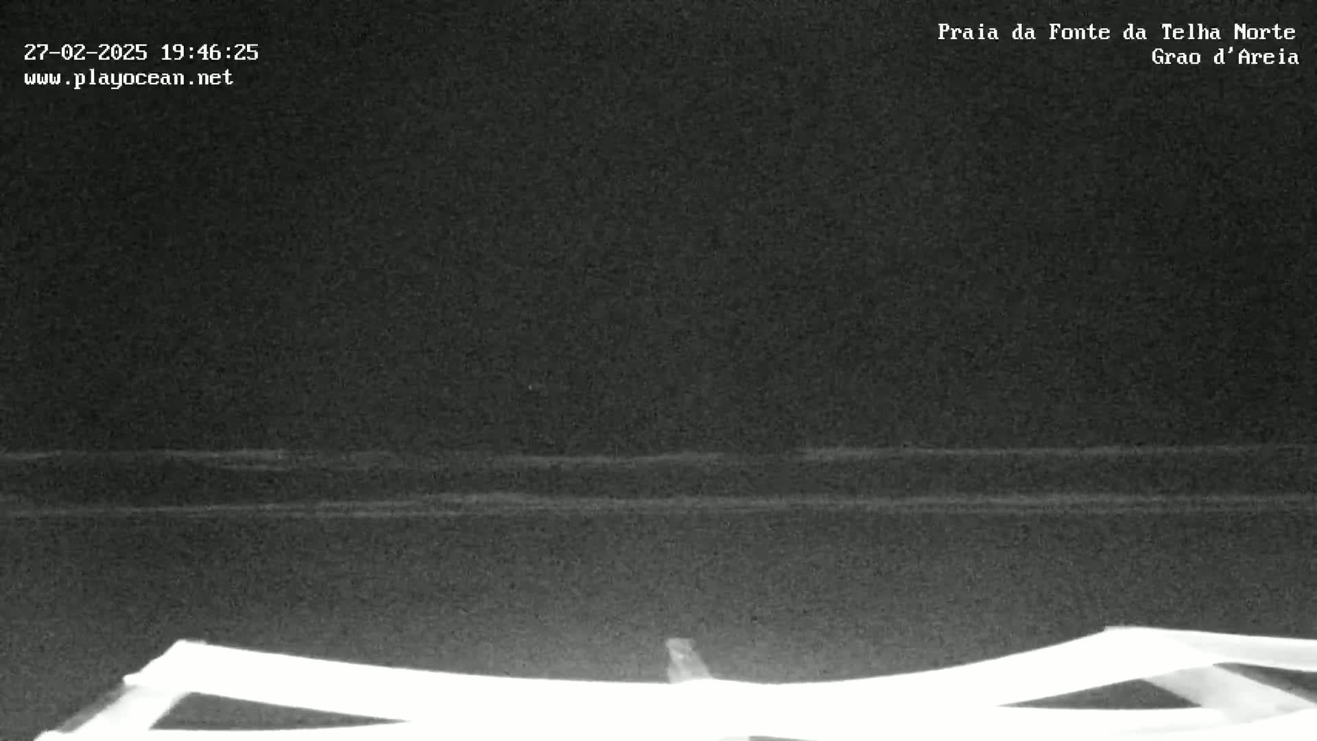 A nighttime, low-light image shows dark water with faint waves lapping on a shore, viewed from a low vantage point.