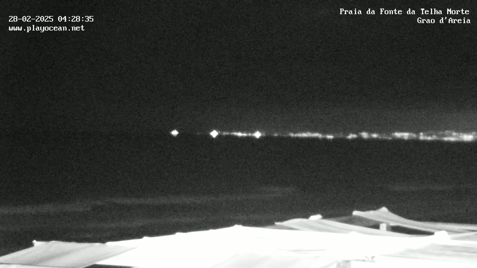 A nighttime, low-light view of a dark body of water with a distant, faintly lit shoreline and several dark, covered structures in the foreground.