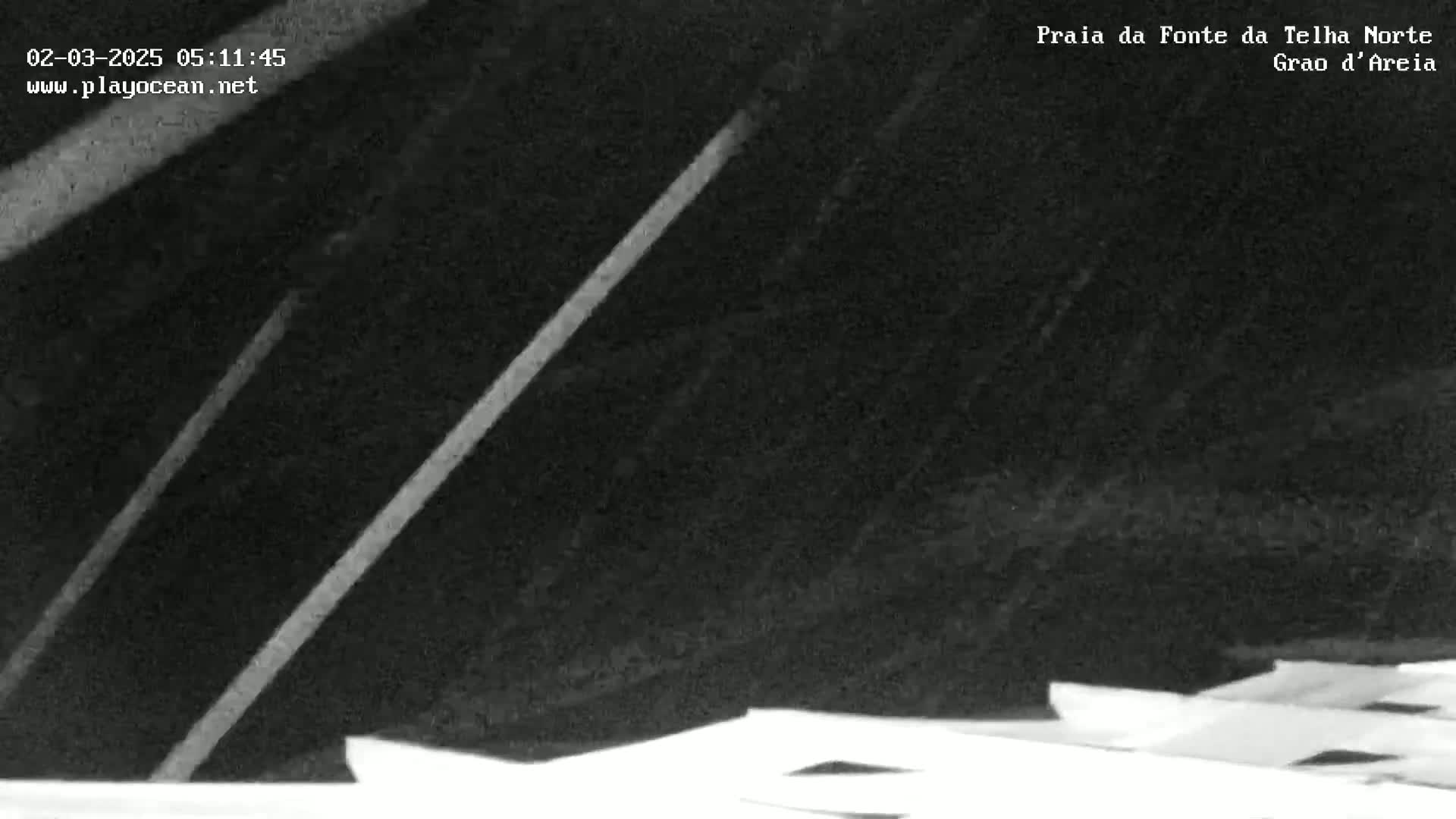 A low-light, grainy image shows two bright diagonal lines against a dark background, possibly a beach at night.