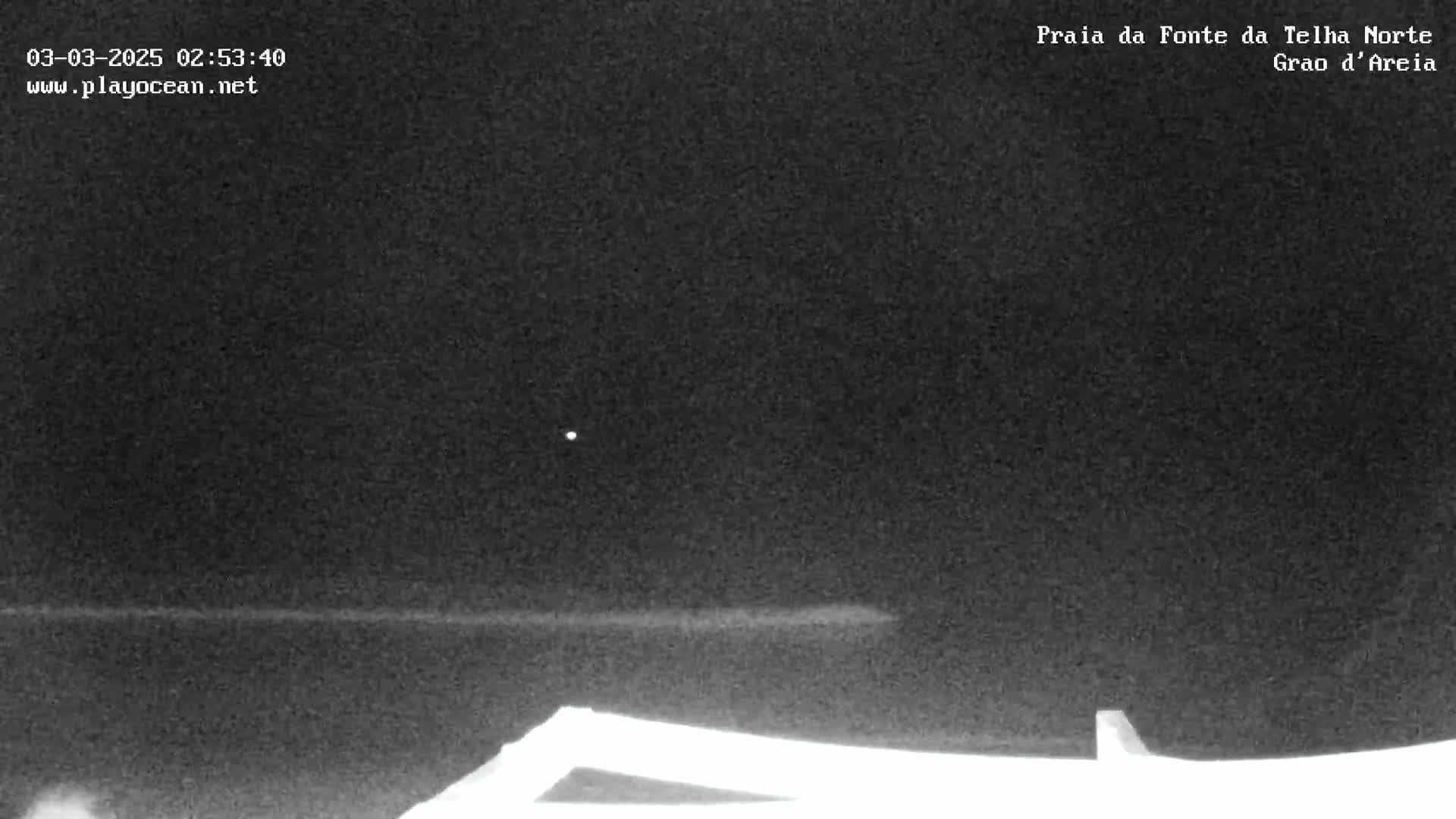 A nighttime, low-light image shows a dark ocean under a dark sky with a single bright light visible.