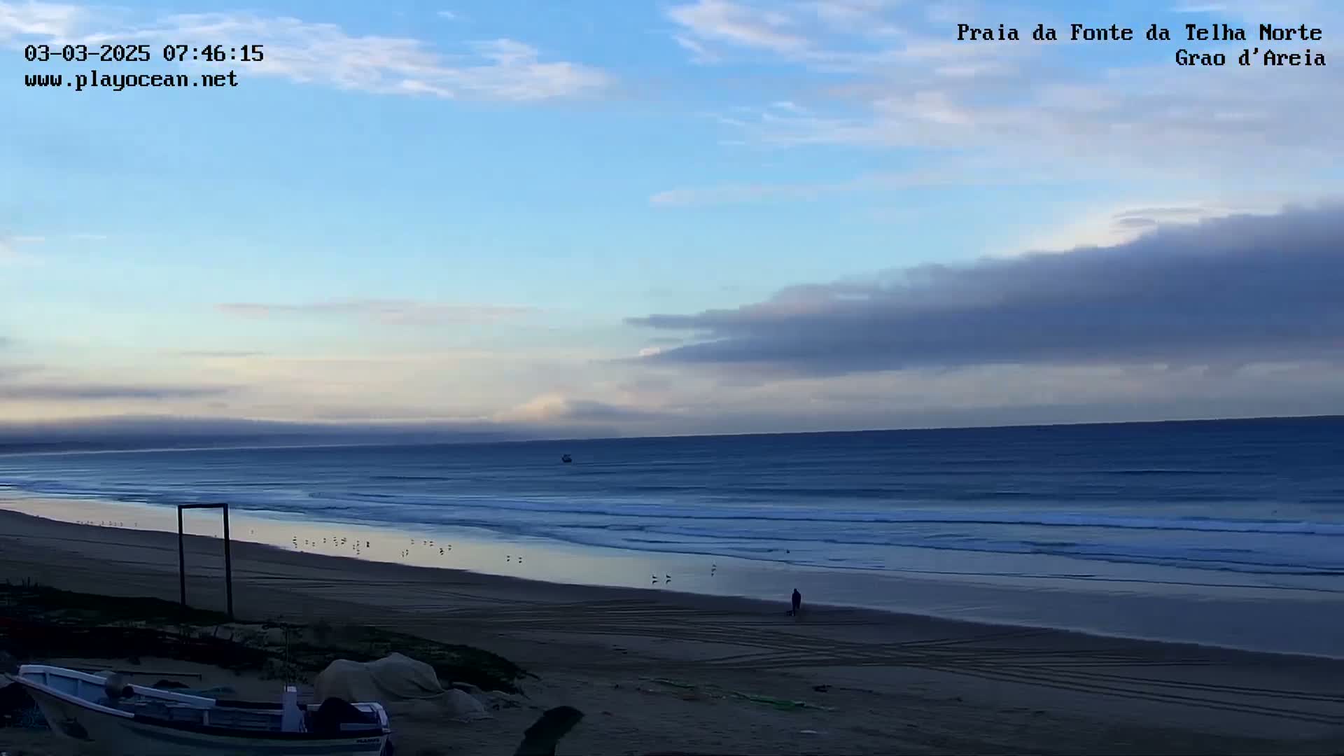 A sandy beach stretches out to a calm ocean under a partly cloudy sky.
