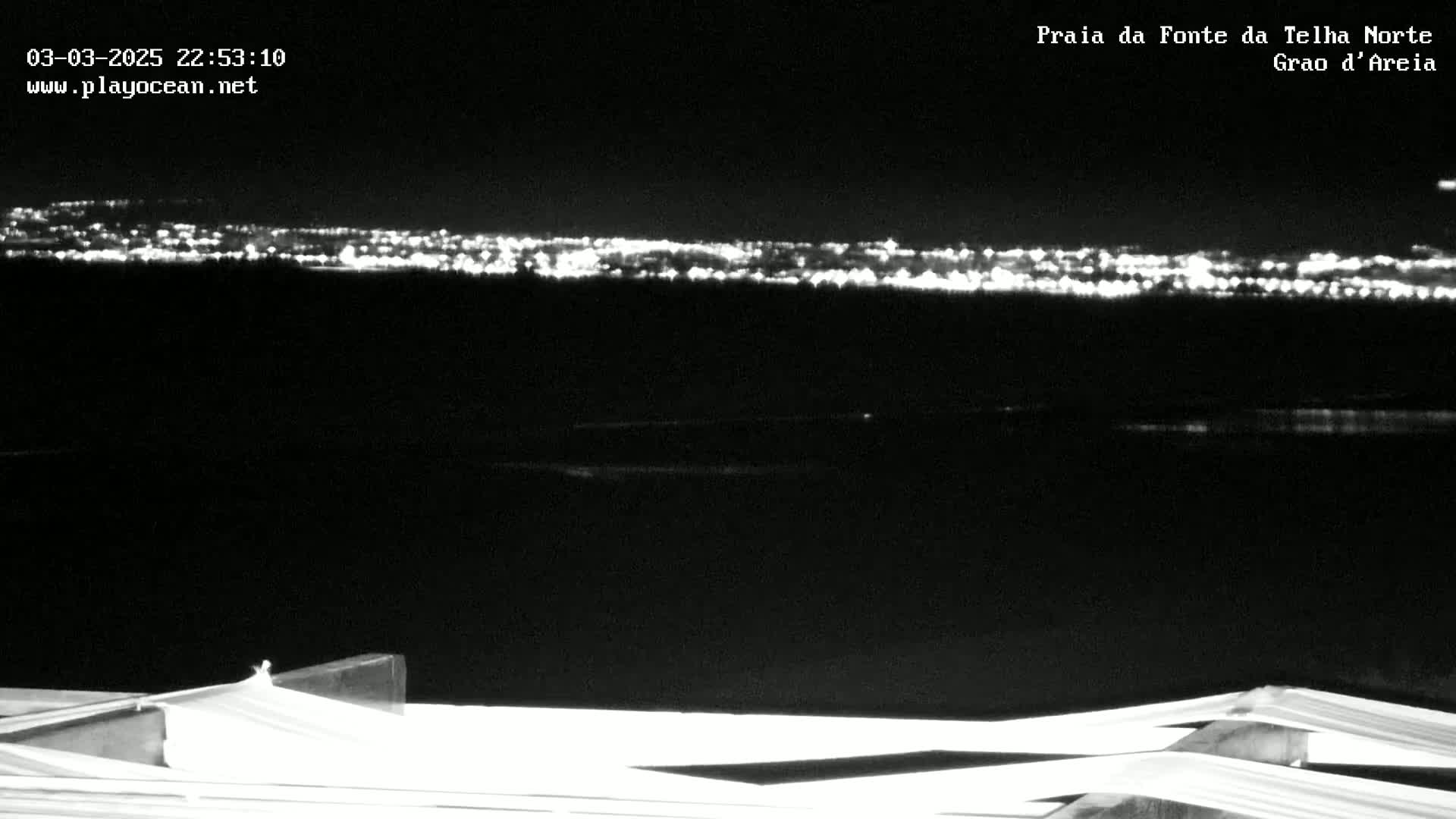 A nighttime, long-range view shows a distant city skyline illuminated against a dark sky, with a portion of a white structure in the foreground.