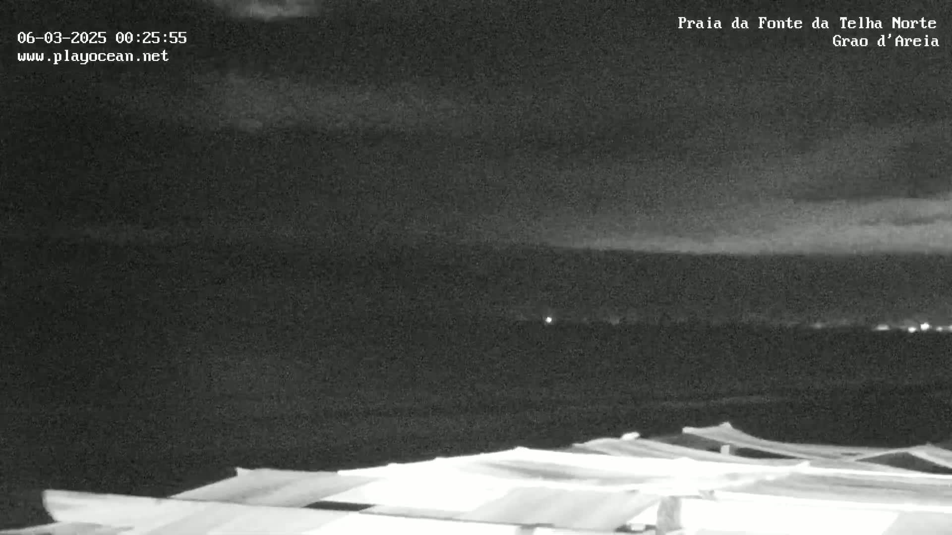 A nighttime, low-light view shows a dark, cloudy sky over a beach with several white, covered structures in the foreground.
