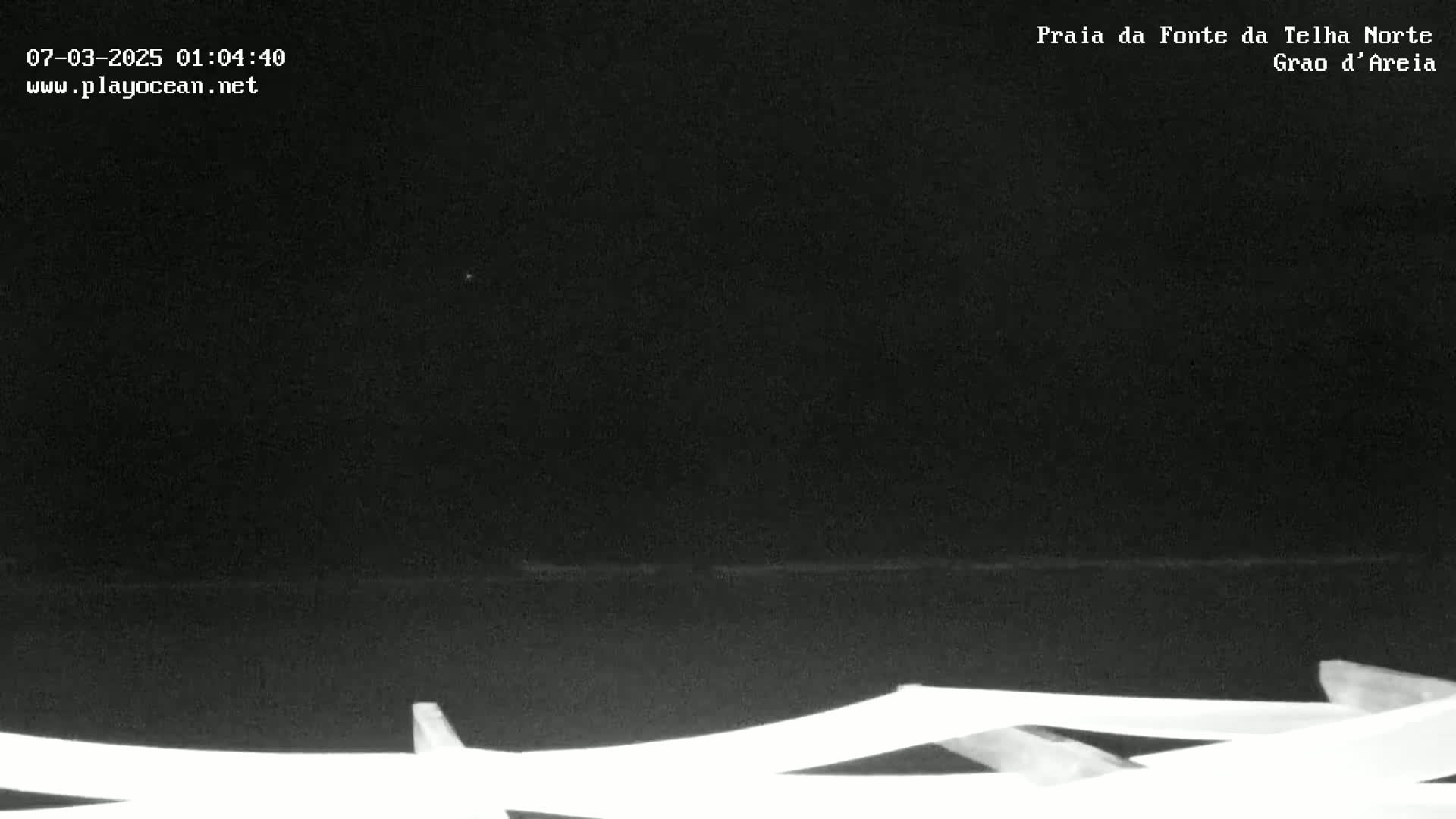 A nighttime, low-light view of a dark ocean, with white structures in the foreground.