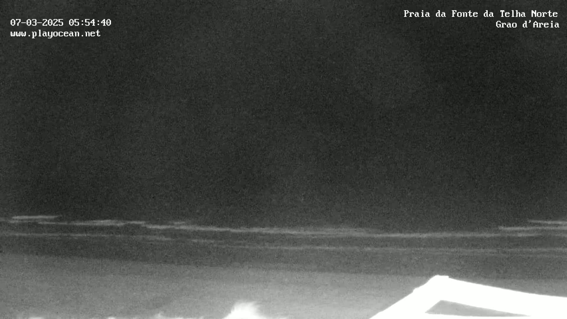 A nighttime, low-light image shows dark, gently rolling ocean waves under a dark sky.