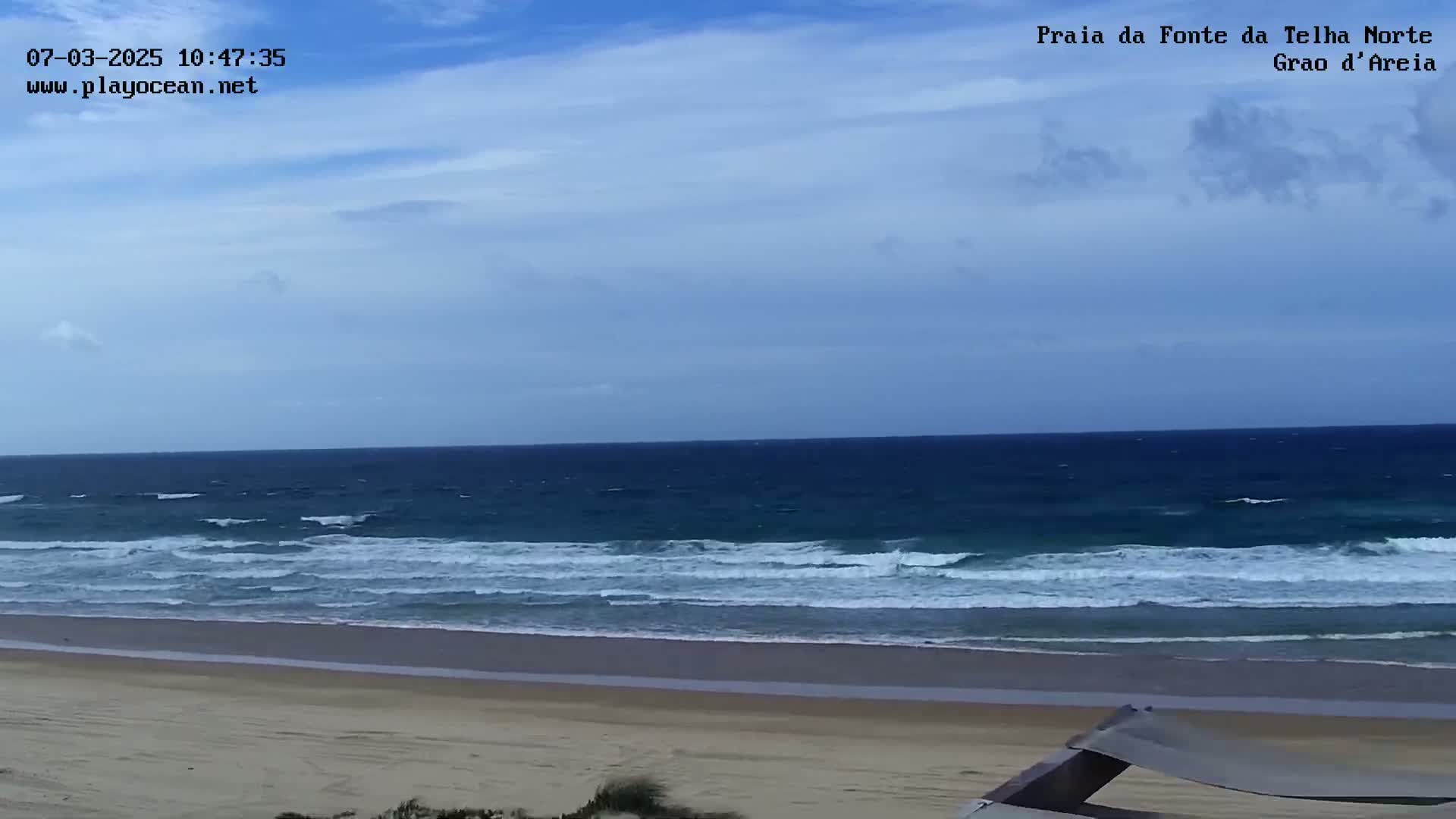 A sandy beach with moderate waves under a partly cloudy sky is shown.