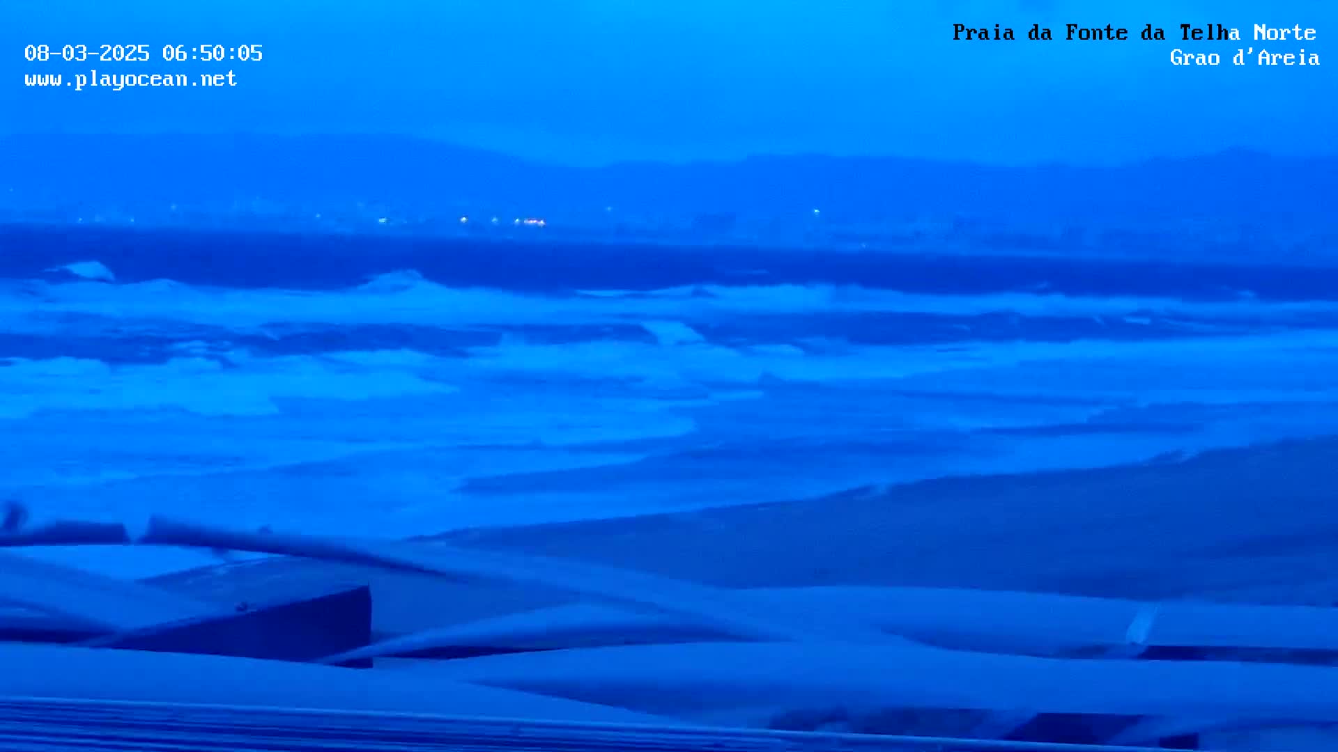 A dark blue ocean with waves crashes on a beach under a twilight sky.