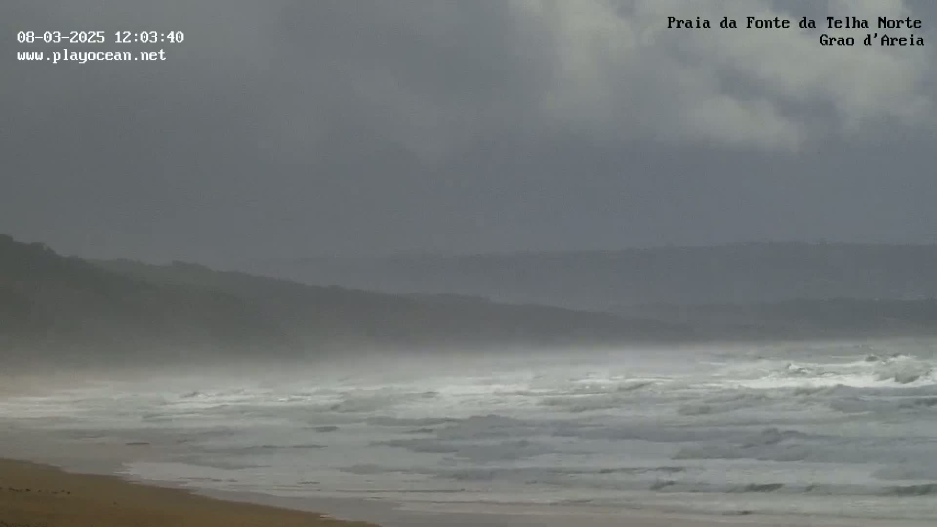 A sandy beach with moderate waves under an overcast sky.