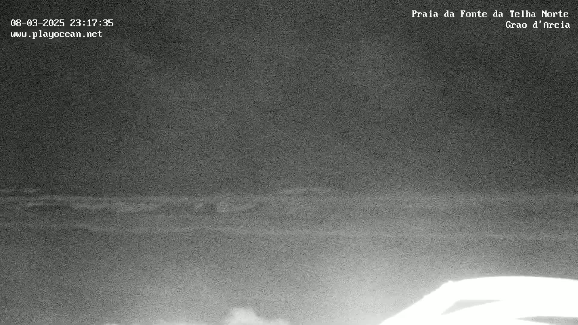 A low-light nighttime image shows a dark, flat ocean under a dark sky.