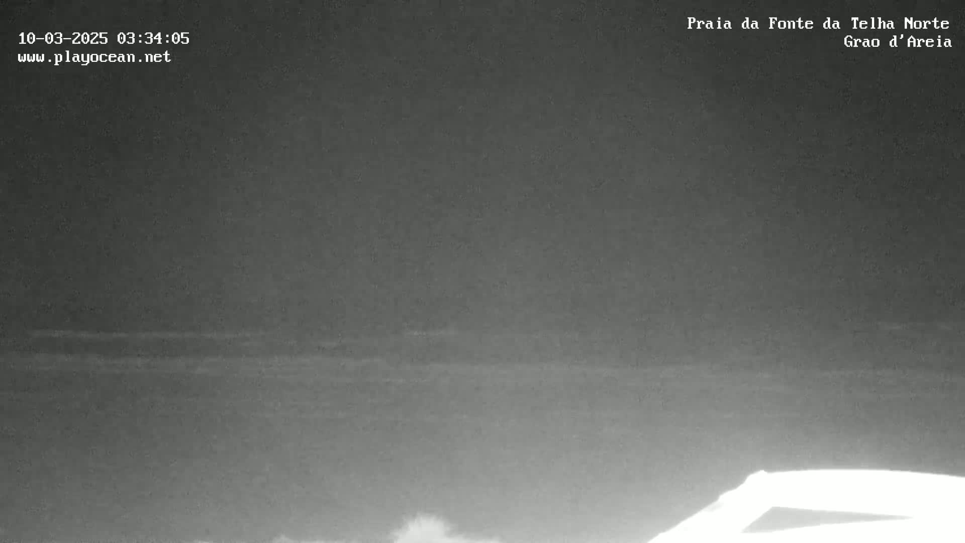 A dark, nighttime view of a calm ocean with a small portion of what appears to be a vehicle visible in the bottom right corner.