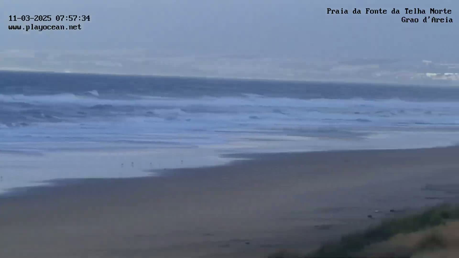 A wide, sandy beach stretches towards a gray, overcast sky and a somewhat choppy ocean with small waves.