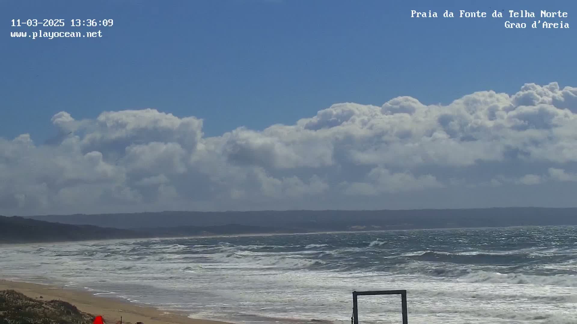 A sandy beach with choppy ocean waves under a partly cloudy sky.
