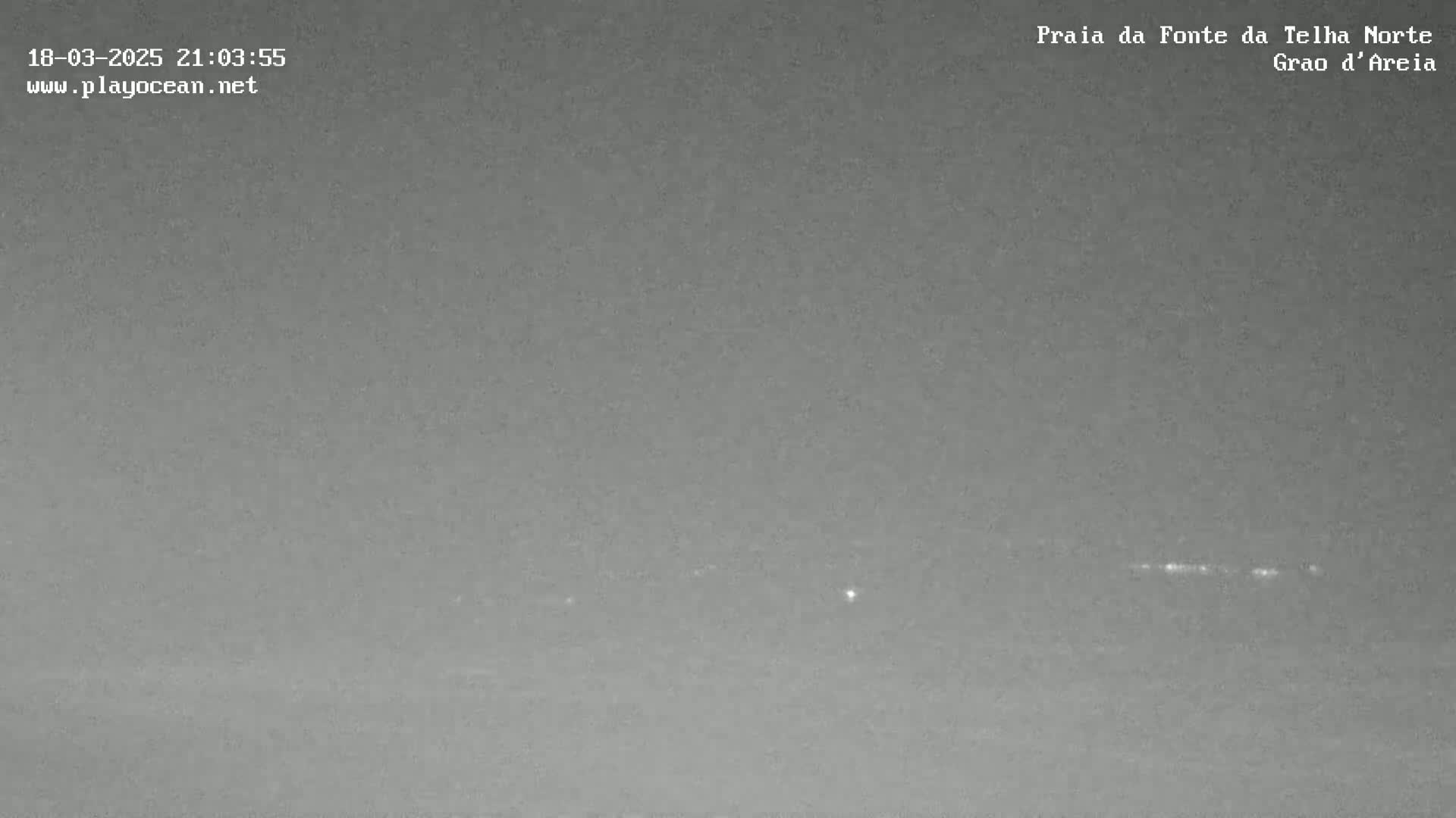 A nighttime, low-light image shows a dark, flat landscape with a faint line of lights on the horizon.