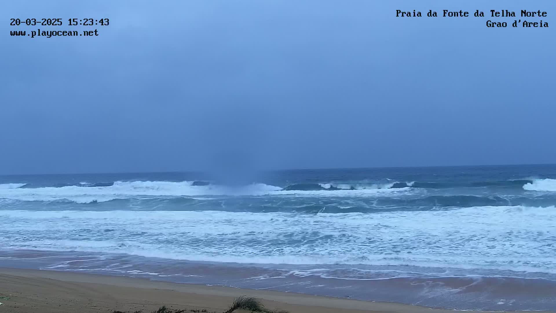 A sandy beach with moderately sized waves rolling onto the shore under an overcast sky.