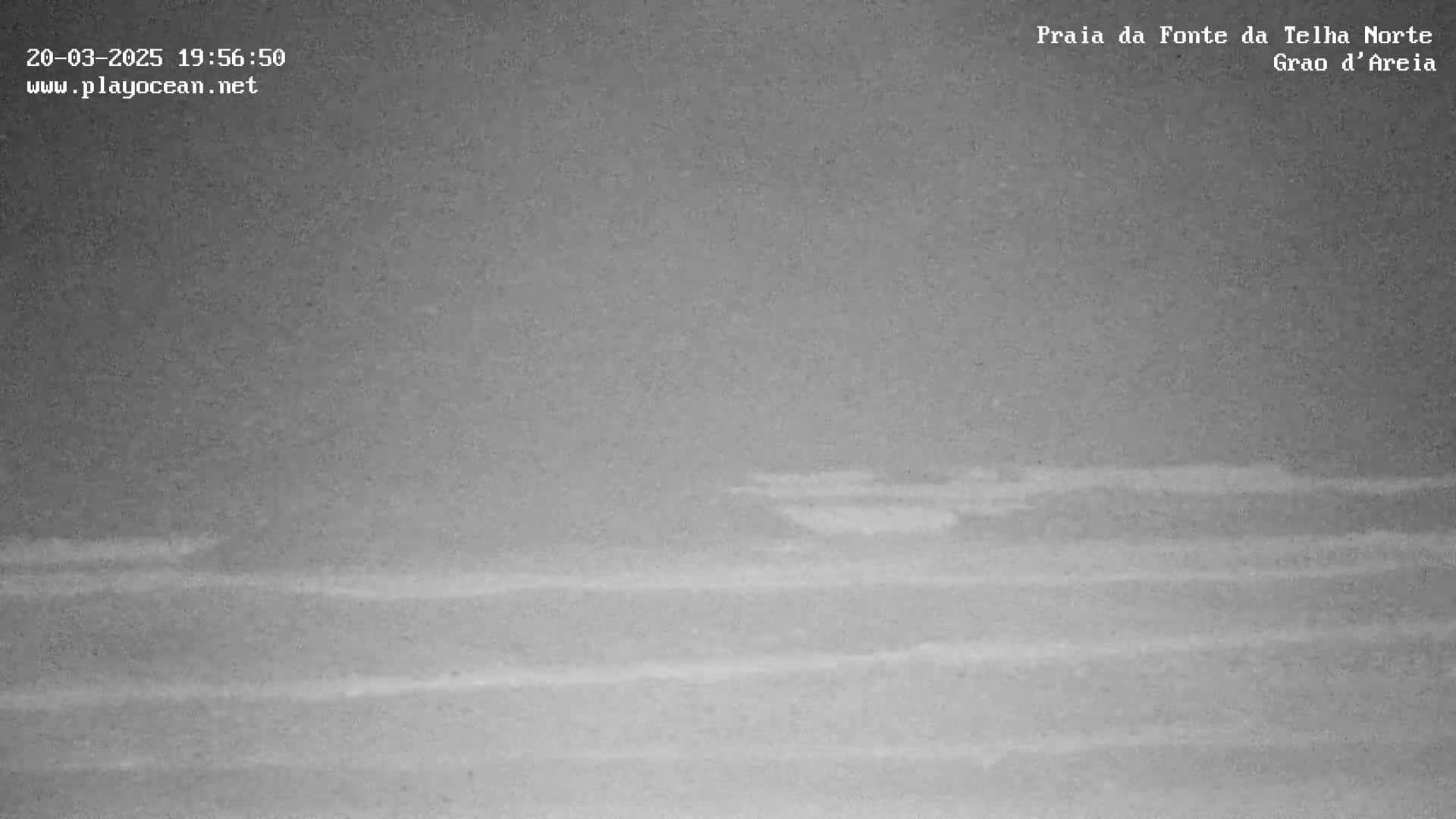 A low-light, nighttime image shows a dark, relatively calm ocean with faint waves under an overcast sky.