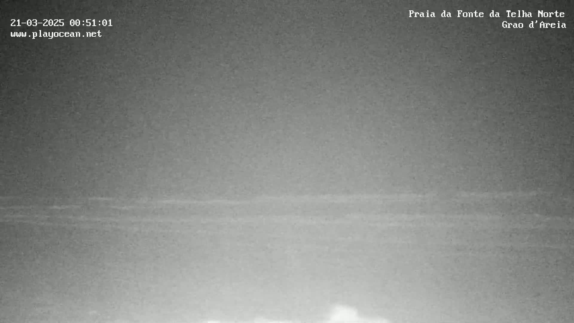 A nighttime, low-light image shows a dark, mostly featureless expanse of ocean with a faint horizon line.