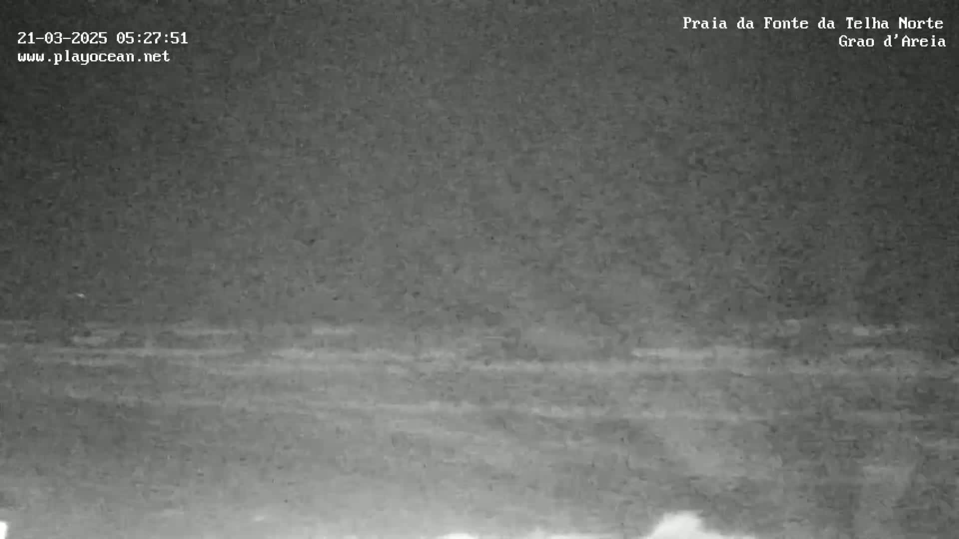 A dark, nighttime view of a beach with a mostly calm ocean under a cloudy sky.
