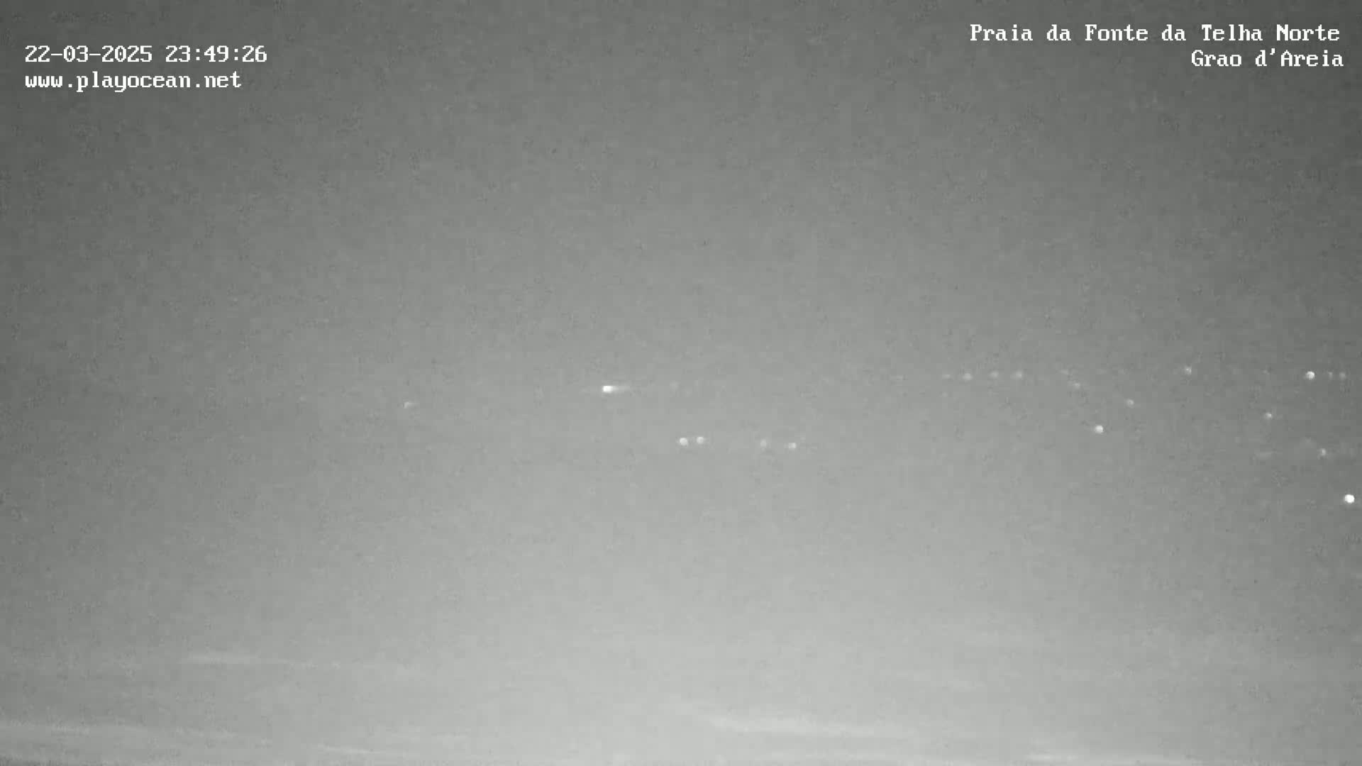 A nighttime, overcast view shows a distant line of faint lights on the horizon.