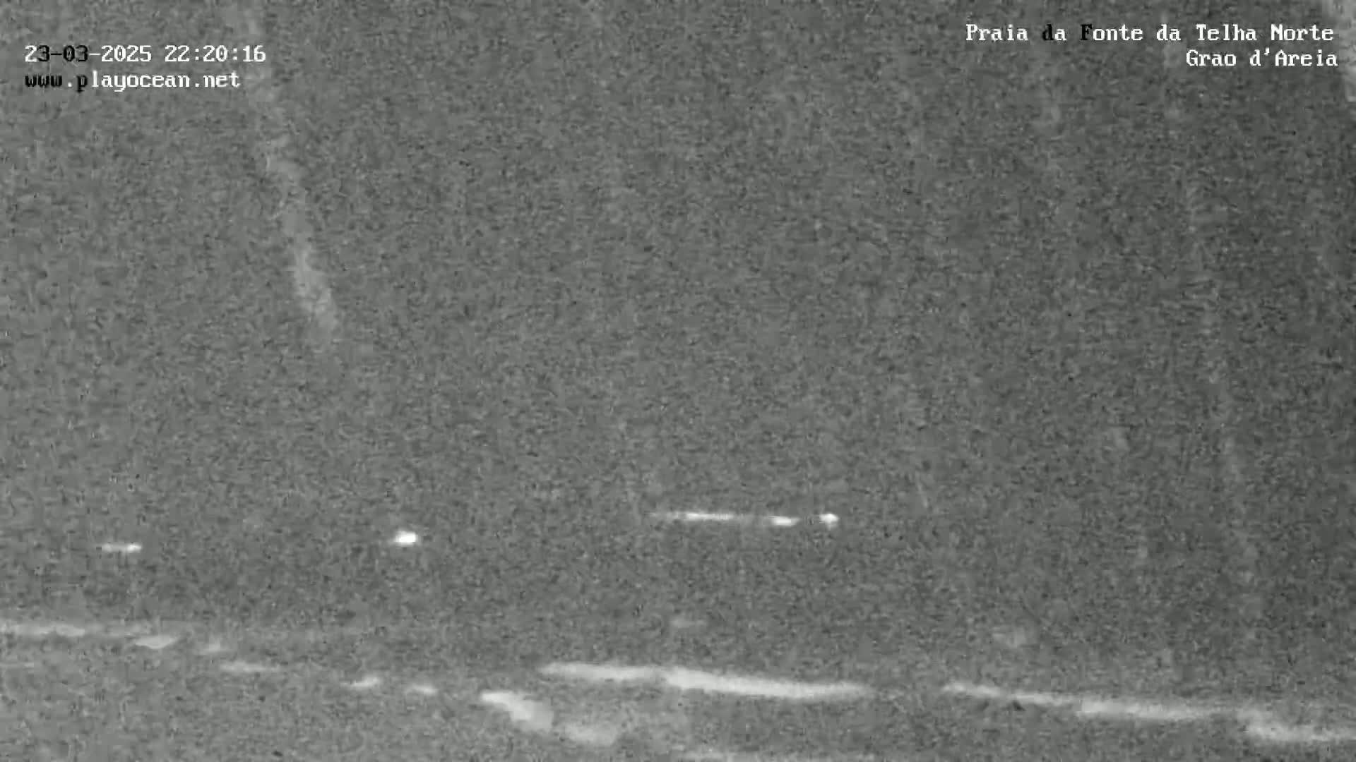 A nighttime, low-light image shows a dark, possibly sandy or gravelly, expanse under a slightly snowy or hazy sky.