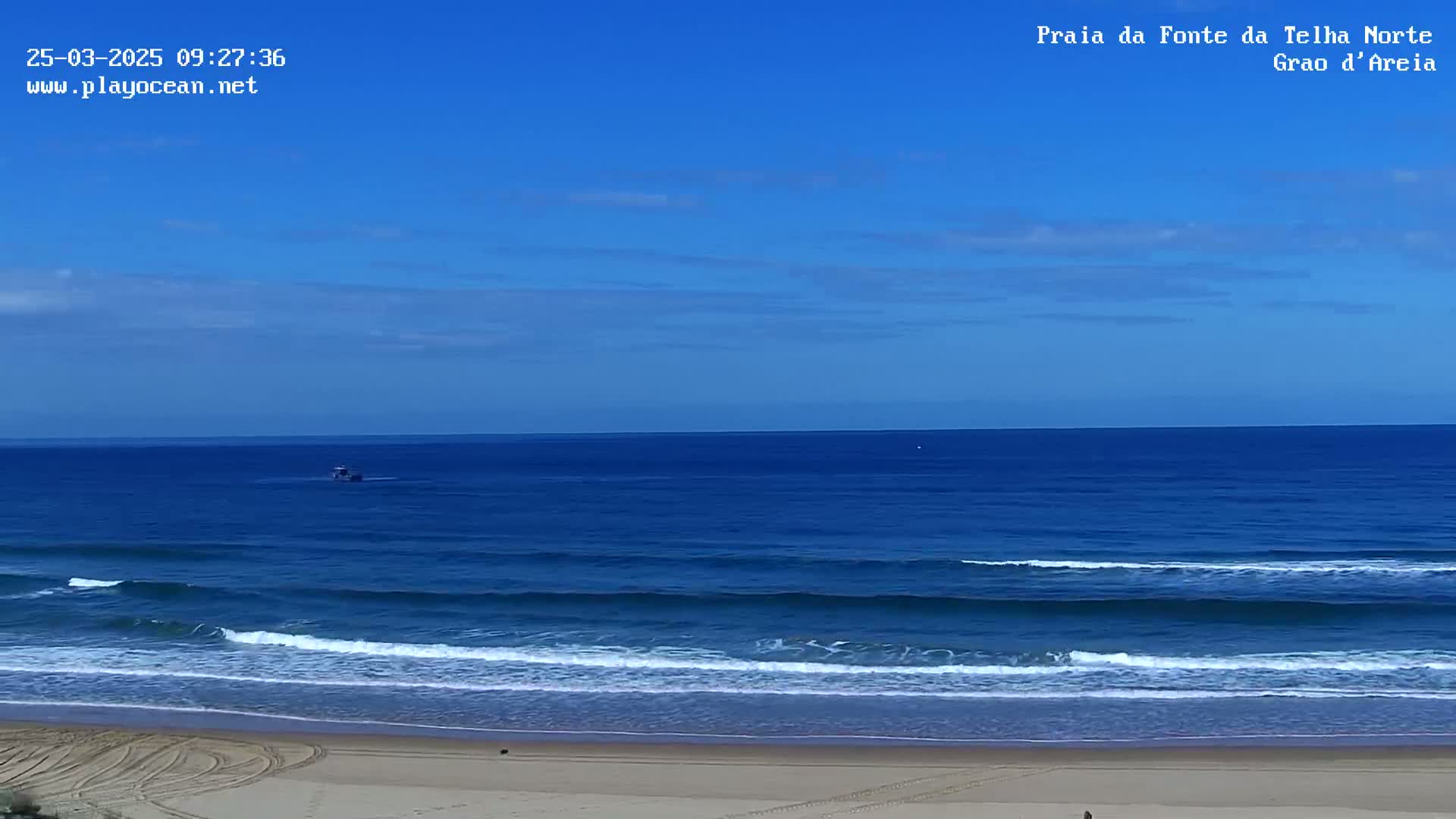 A sandy beach with gentle waves rolls onto the shore under a clear blue sky.