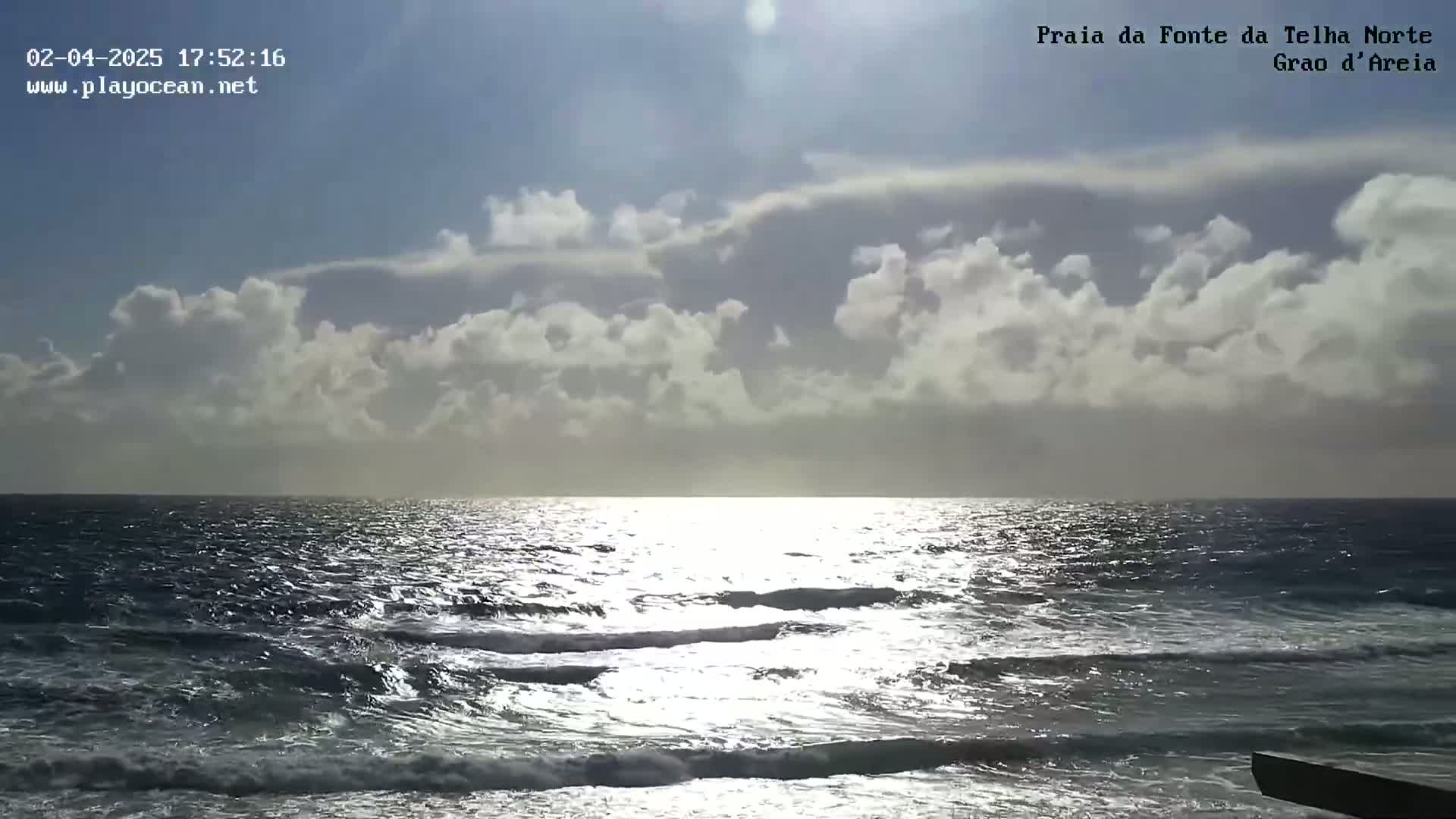 A partly cloudy sky over a wavy ocean reflects sunlight on the water.