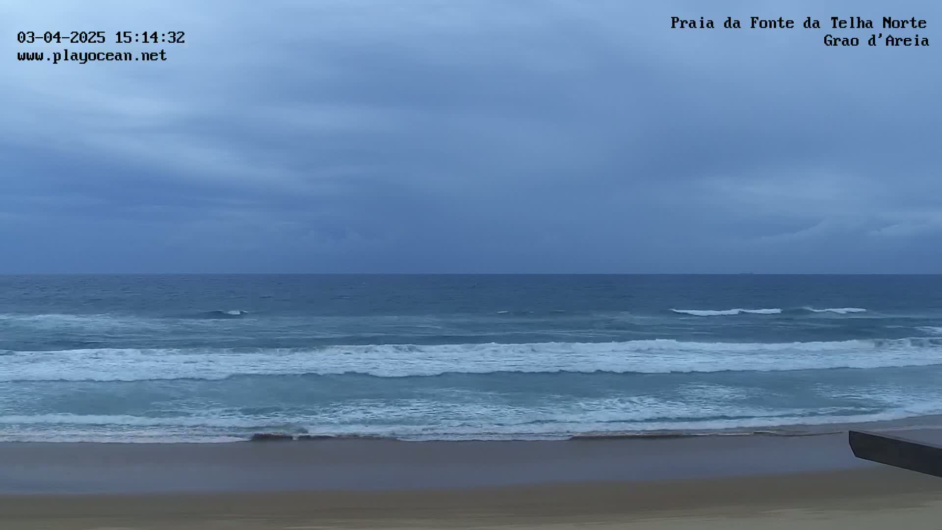 A sandy beach meets a somewhat choppy ocean under an overcast sky.