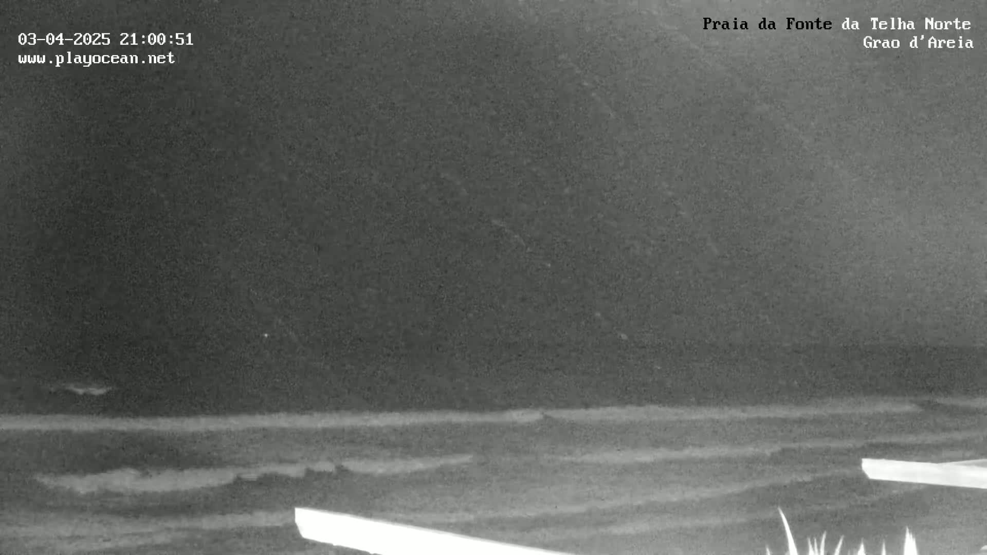 A nighttime, low-light view of a dark ocean with small waves gently lapping the shore.