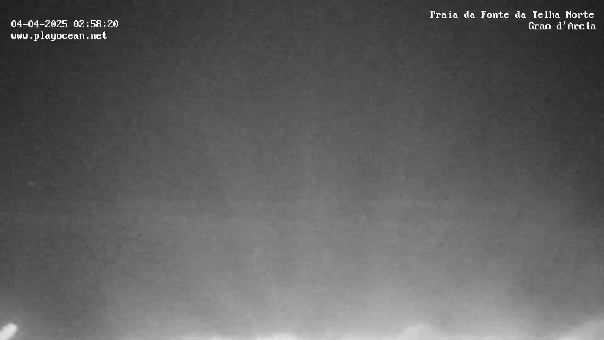 A low-light nighttime image shows a dark, overcast sky over what appears to be a beach or coastal area.