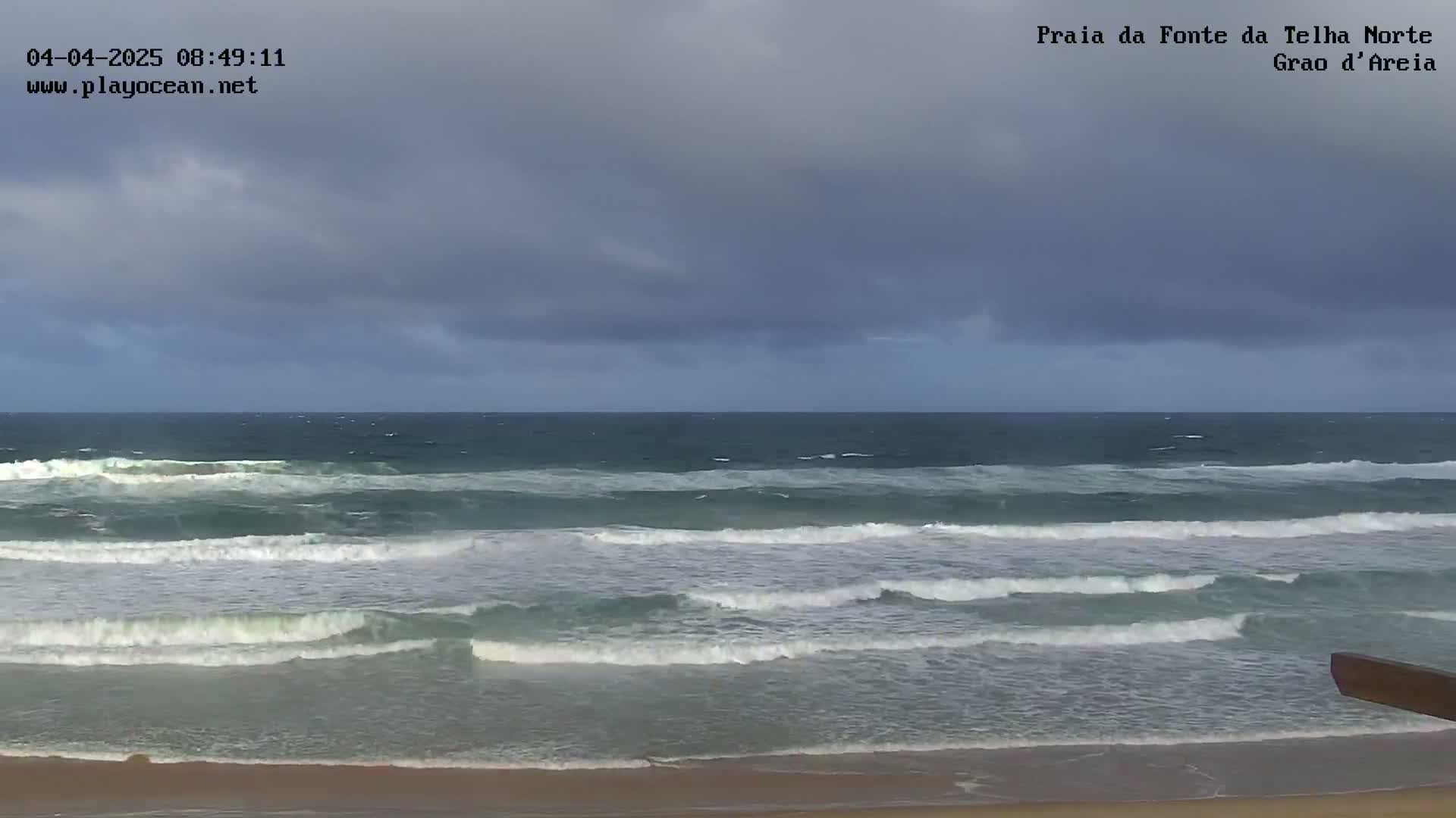 A sandy beach with moderate waves under an overcast sky.