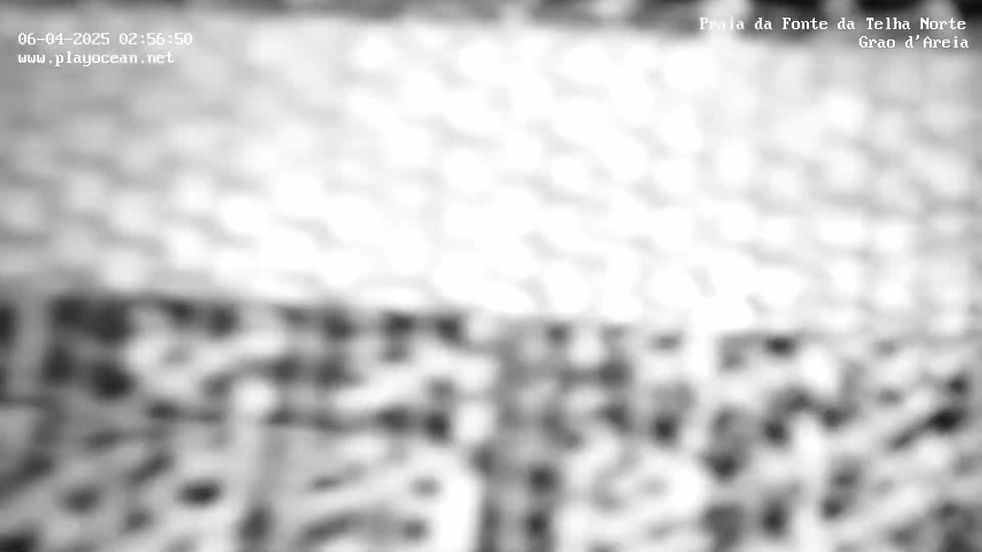 A blurry grayscale image shows an indistinct outdoor scene, possibly a beach, under bright, overcast conditions.