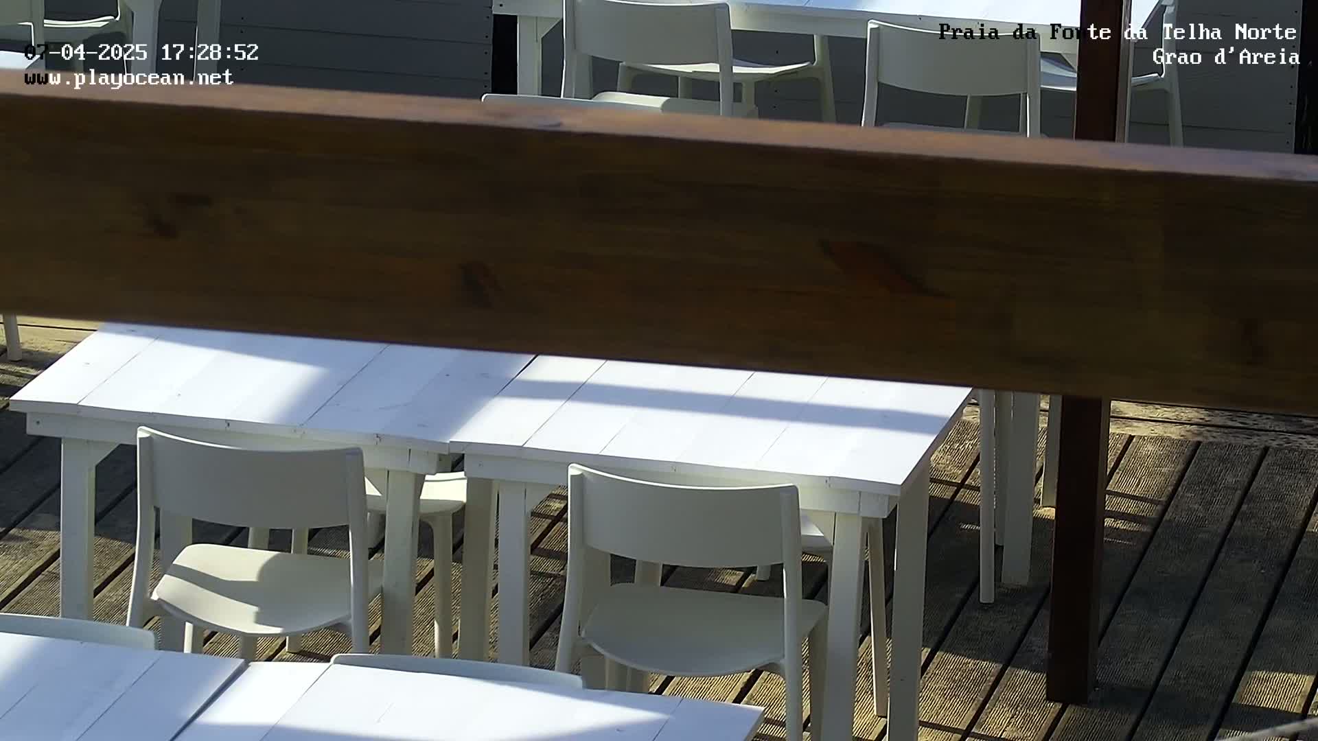 A sunny outdoor patio with several white tables and chairs.