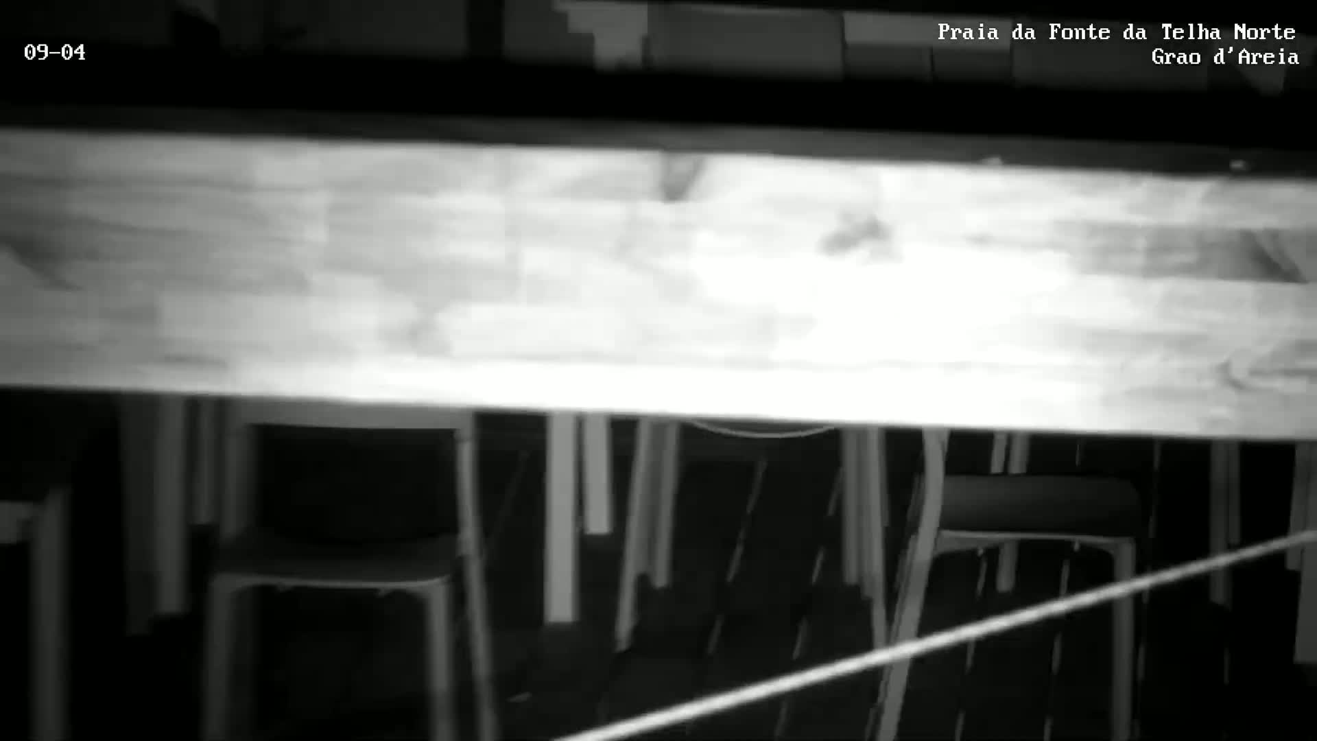 A low-light, black and white image shows a long table above several chairs in a dark room.