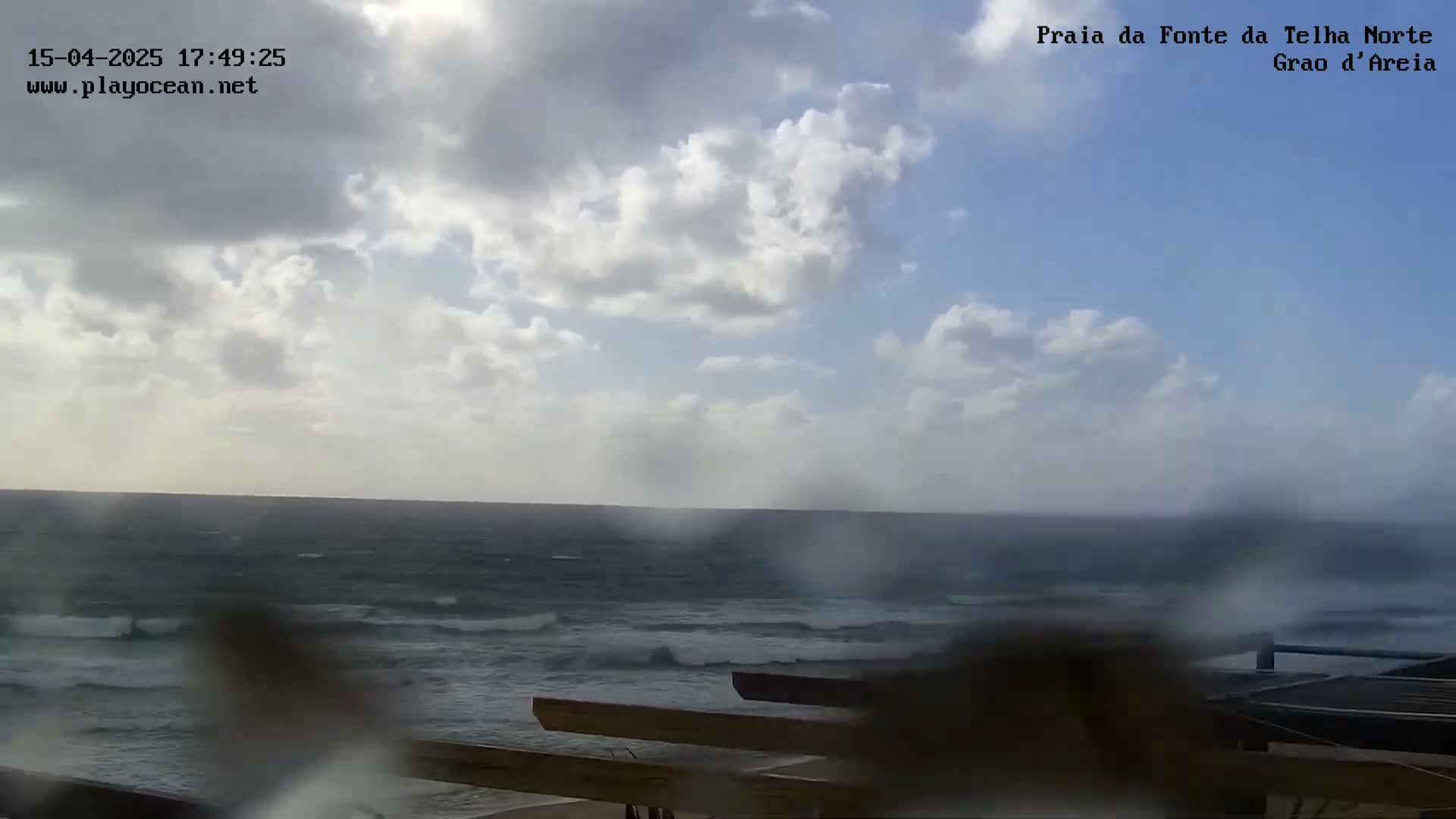 A partly cloudy day with a choppy ocean seen from behind a wooden structure.