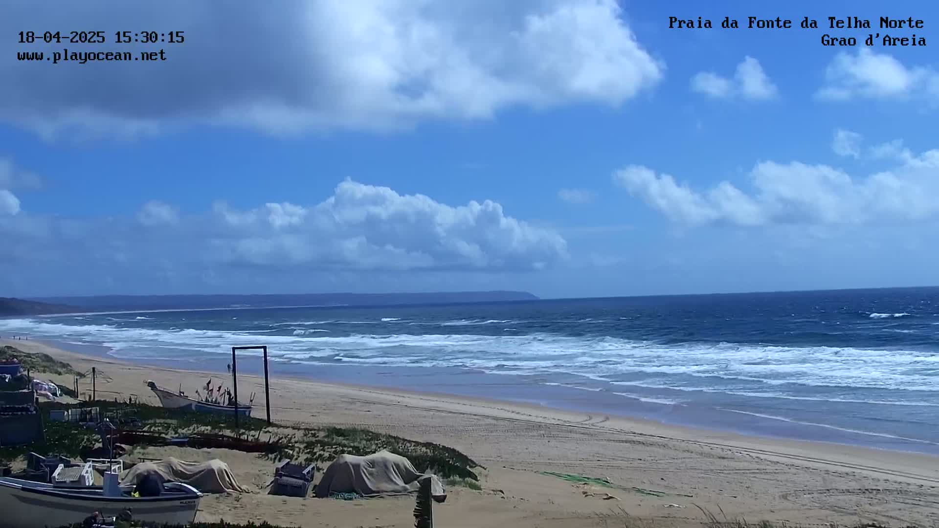 A sandy beach with several small boats is visible, with a partly cloudy sky and a somewhat choppy ocean in the background.