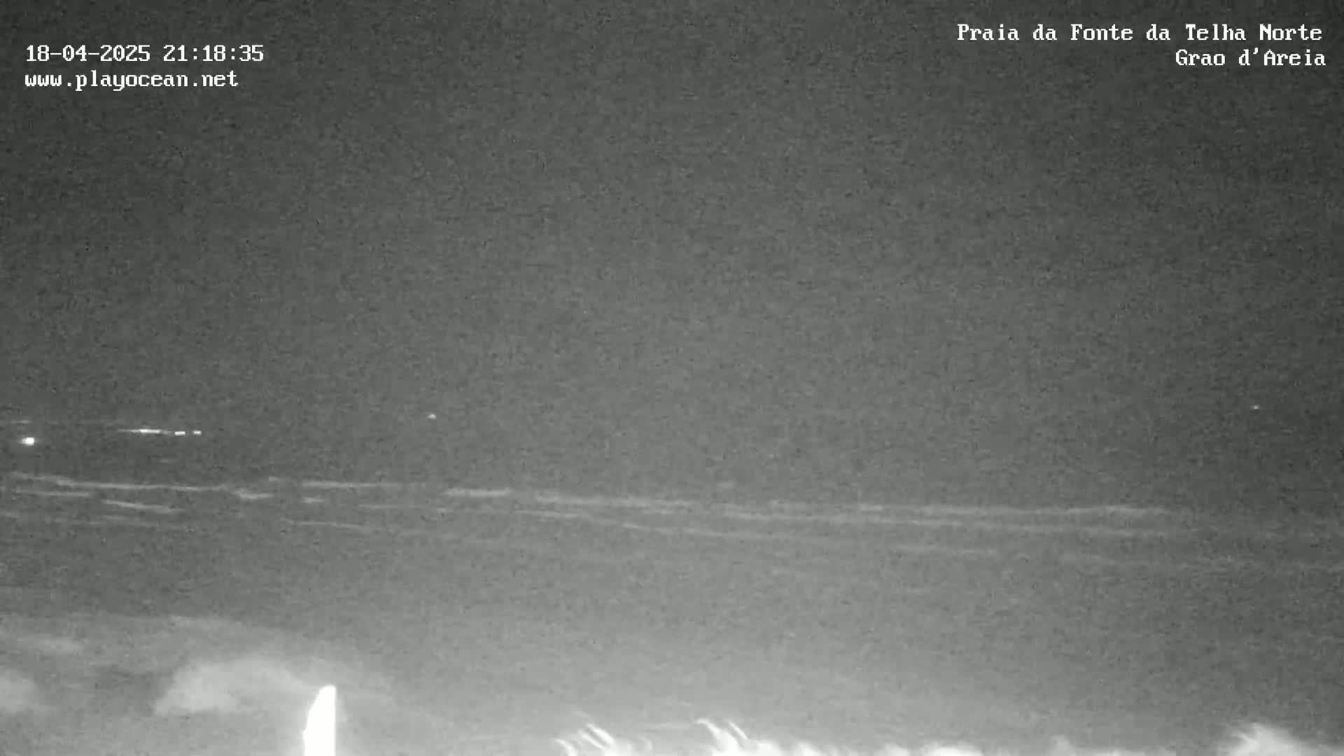 A nighttime view of a dark ocean with small waves under a clear, dark sky.
