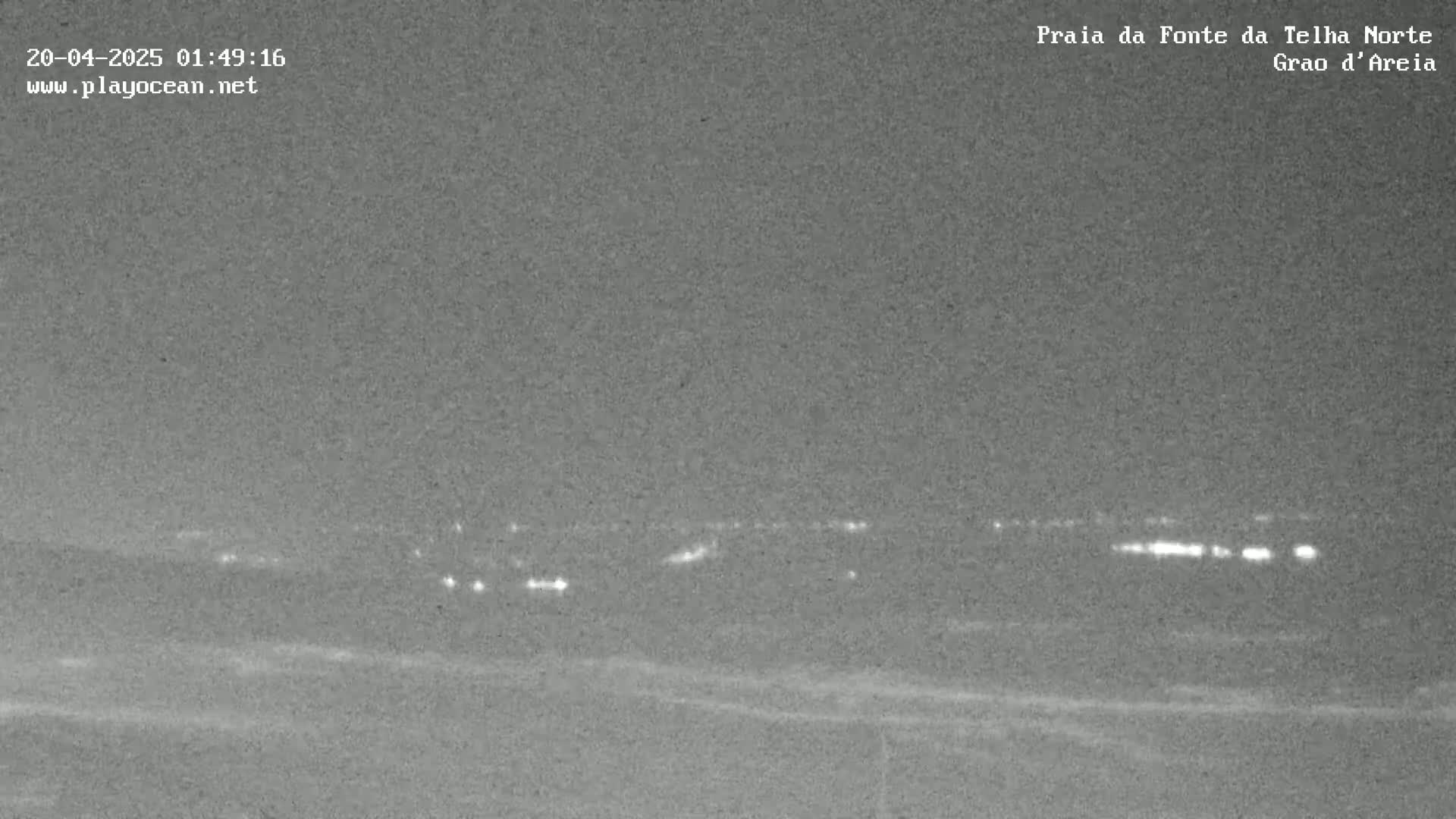 A nighttime low-light image shows a distant line of lights across a dark, seemingly flat landscape.