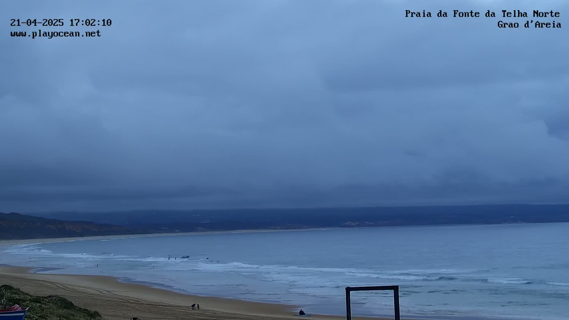 A wide, sandy beach meets a calm, gray ocean under an overcast sky.