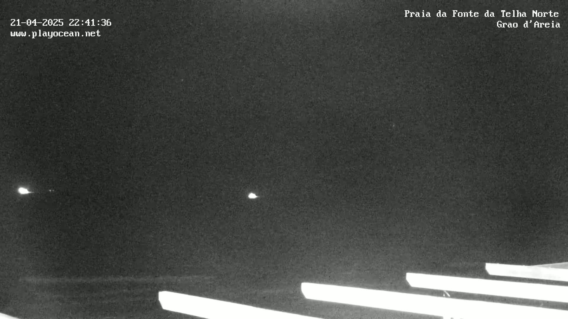 A nighttime, low-light view shows a dark beach with several long, bright white lines extending horizontally across the bottom of the frame.