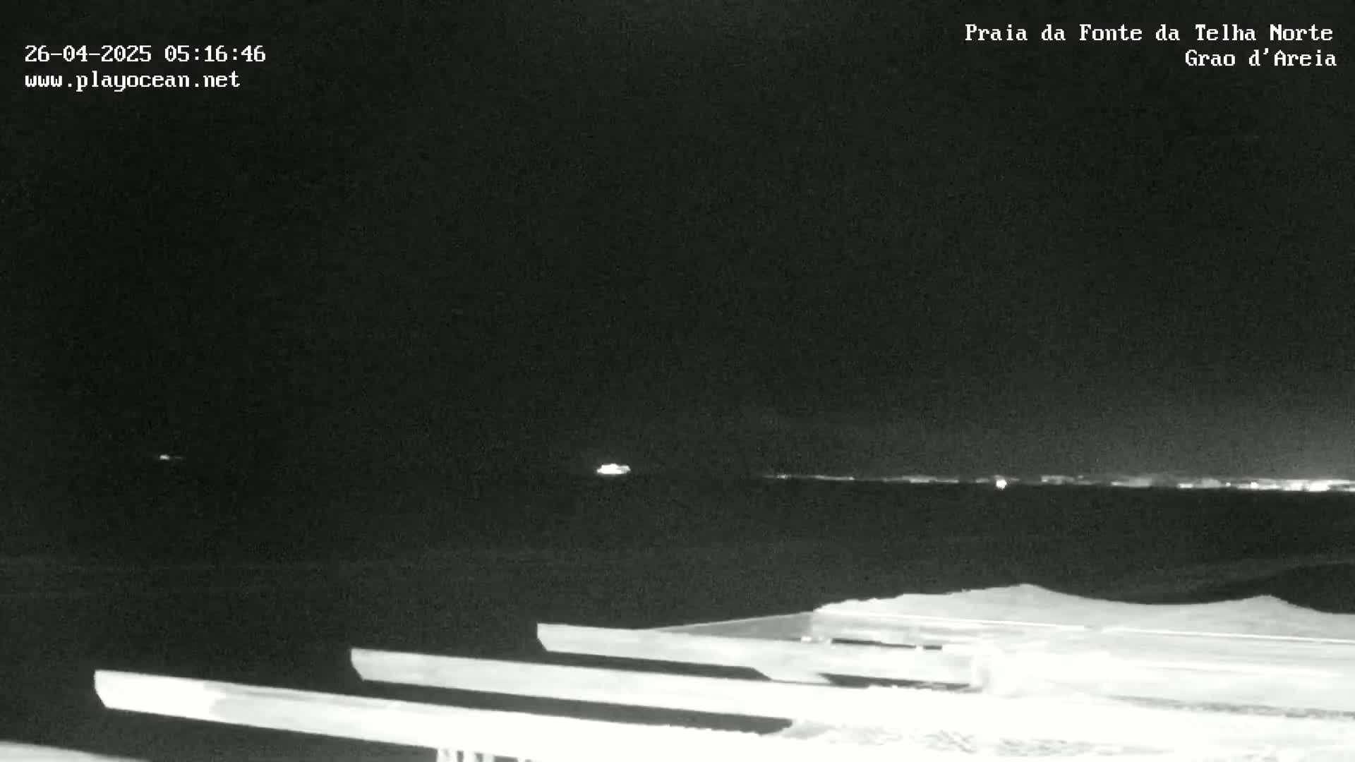 A nighttime view shows a dark body of water with faint lights on the horizon, and a foreground of what appears to be wooden planks or a boardwalk.